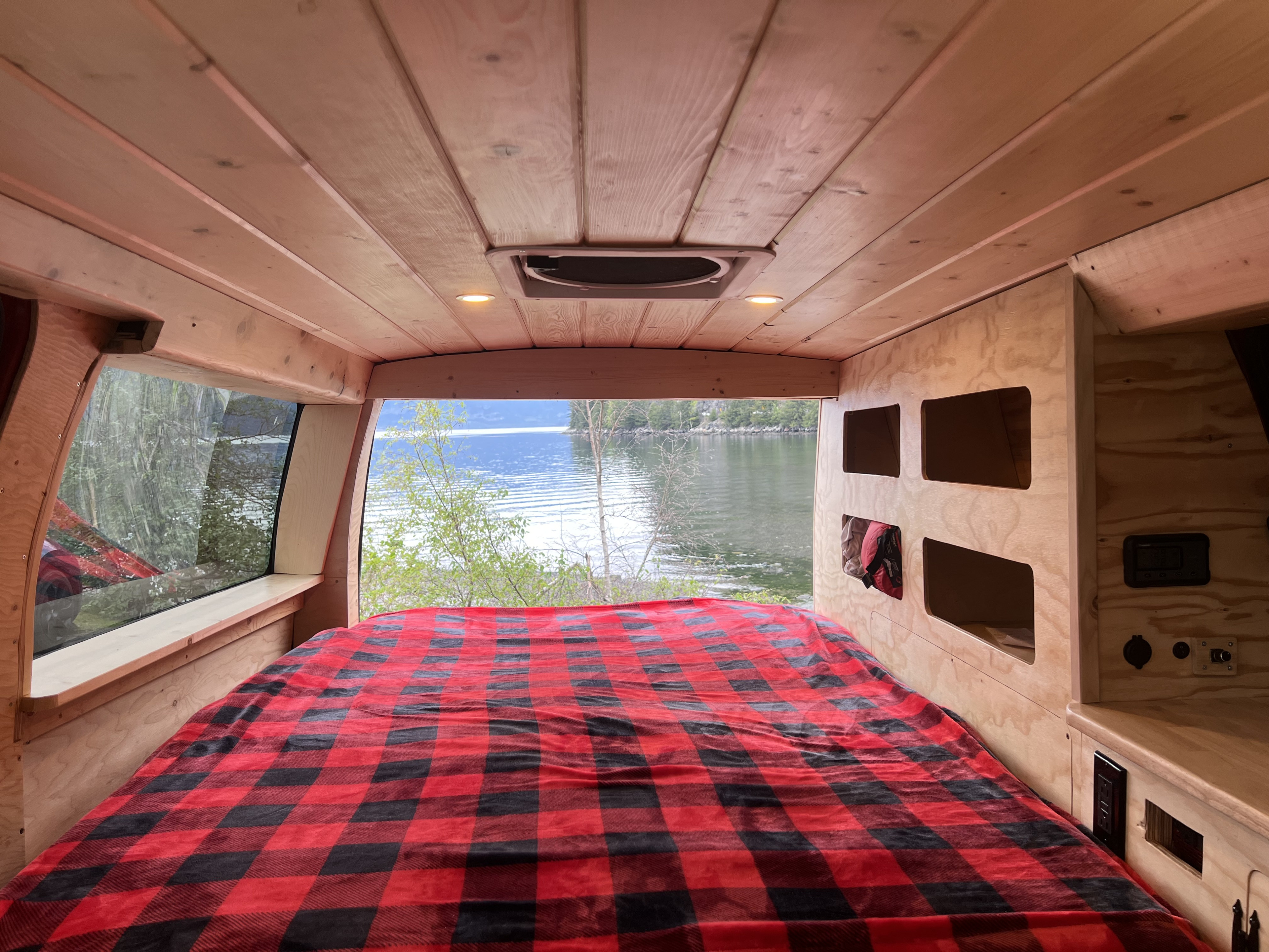 Cozy rv rental interior with a plaid bed and stunning lake view from the large window.. Gmc Savanna 2010
