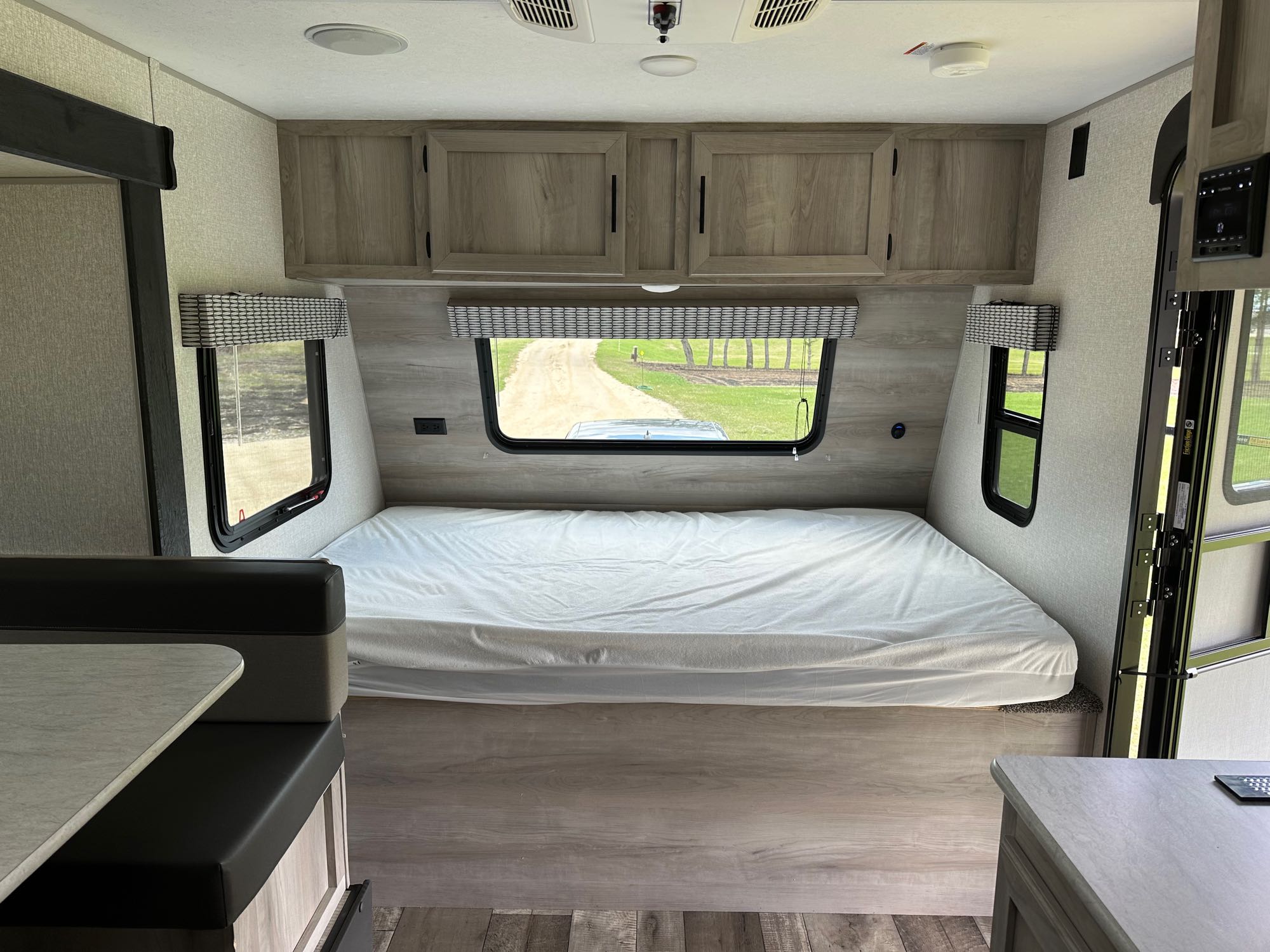 Step inside this RV rental's functional interior: a cozy bed with scenic windows, overhead cabinets, and a dinette on the left.. KZ Sportsman 181BH 2022