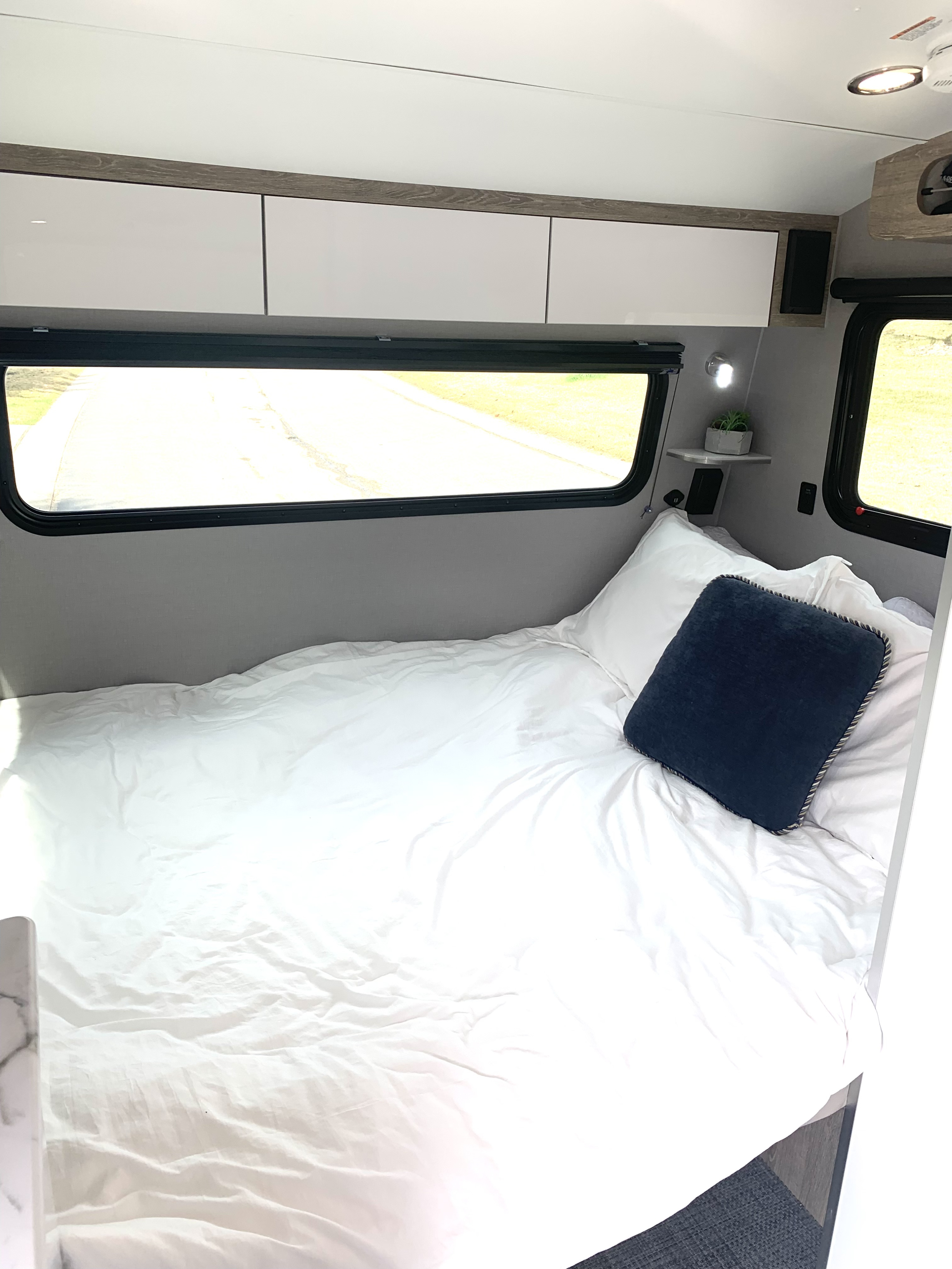 Inside a modern RV rental: a compact sleeping area with crisp white bedding, sleek cabinets, and large windows.. InTech RV Sol 2023