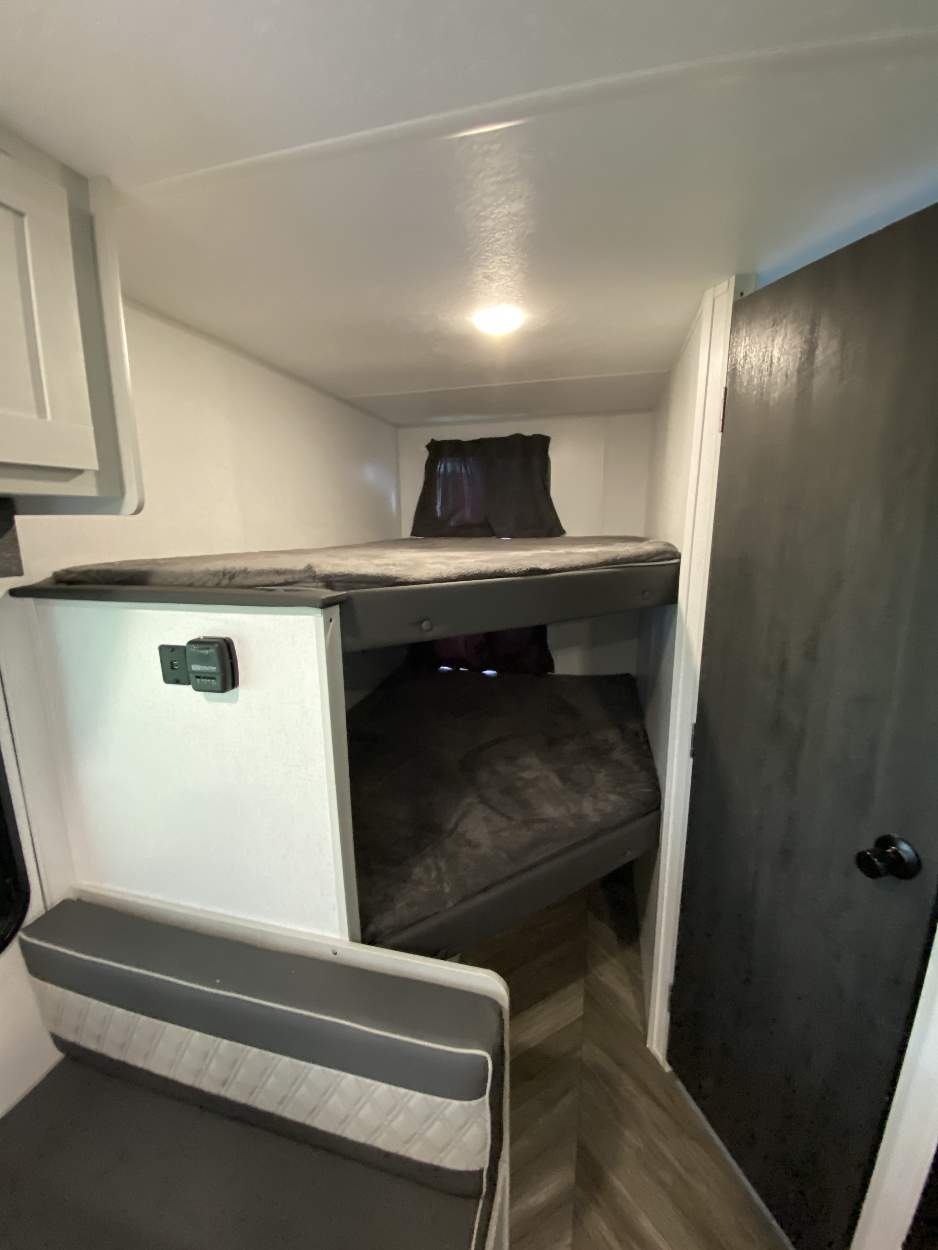 This RV rental features stacked bunk beds with dark bedding, a ceiling light, and an upholstered bench for cozy travel.. Forest River Salem FSX Plantium 2022