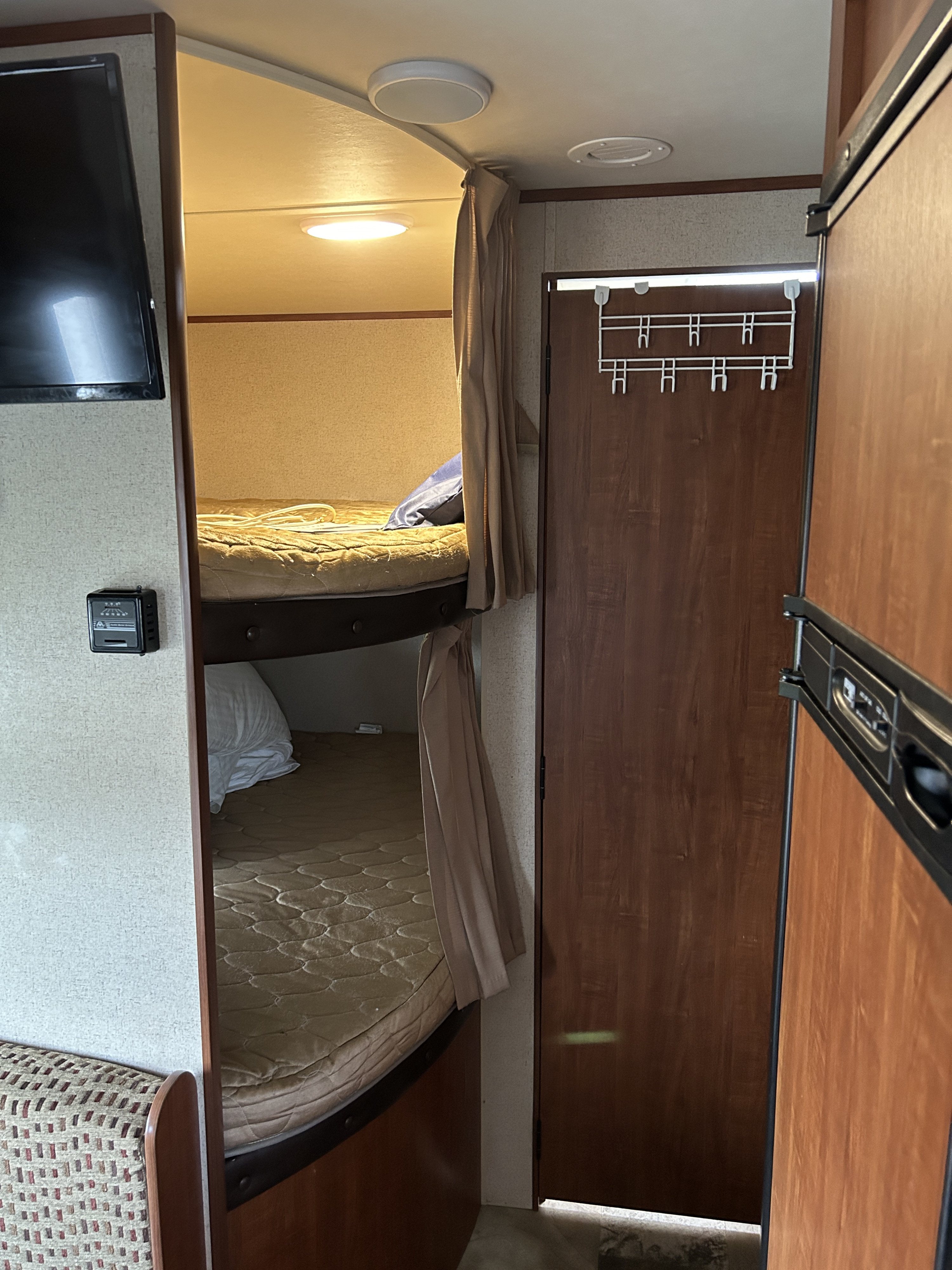 Inside an RV rental: view of bunk beds, TV, thermostat, door with hooks, and refrigerator. Cozy living space.. Jayco Jay Flight SLX 2015