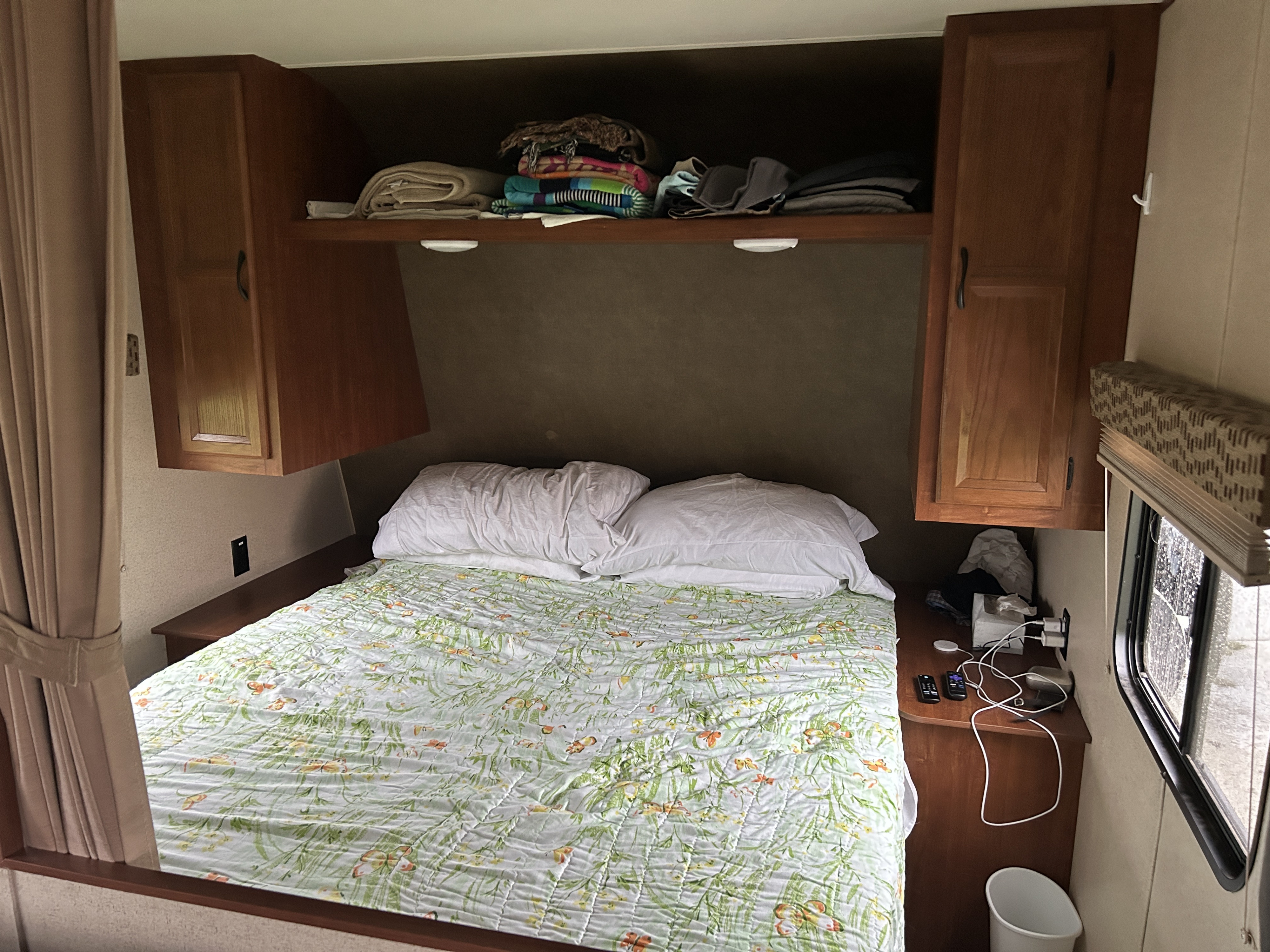 Inside an RV rental, this cozy bedroom features a patterned quilt, overhead cabinets, and convenient bedside amenities.. Jayco Jay Flight SLX 2015