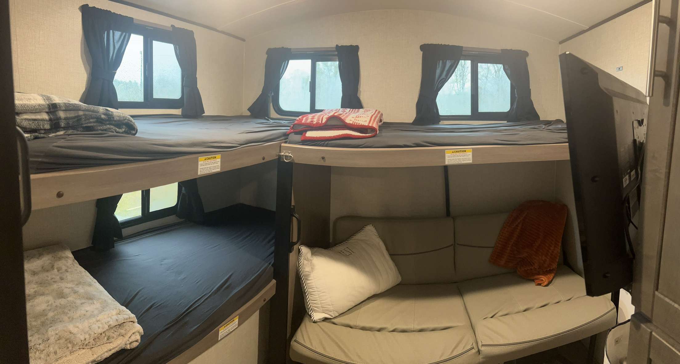 Cozy RV rental bunk room features four beds, a sofa, and mounted TV, ideal for family travel.. Crossroads RV Sunset Trail Super Lite 2022