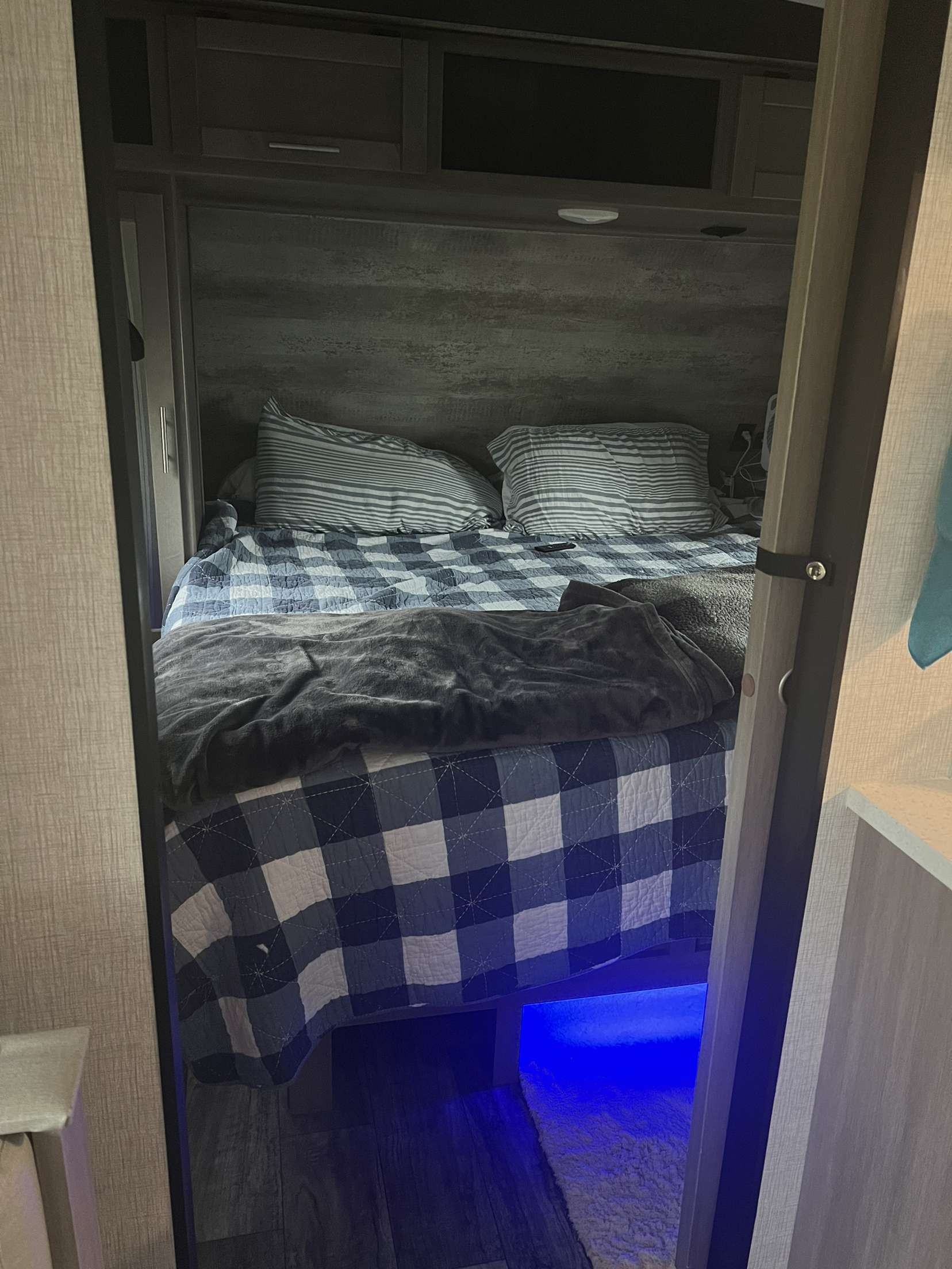 Step inside this cozy RV rental bedroom. Features a bed with blue and white checkered bedding, and soft blue under-bed lighting.. Crossroads RV Sunset Trail Super Lite 2022