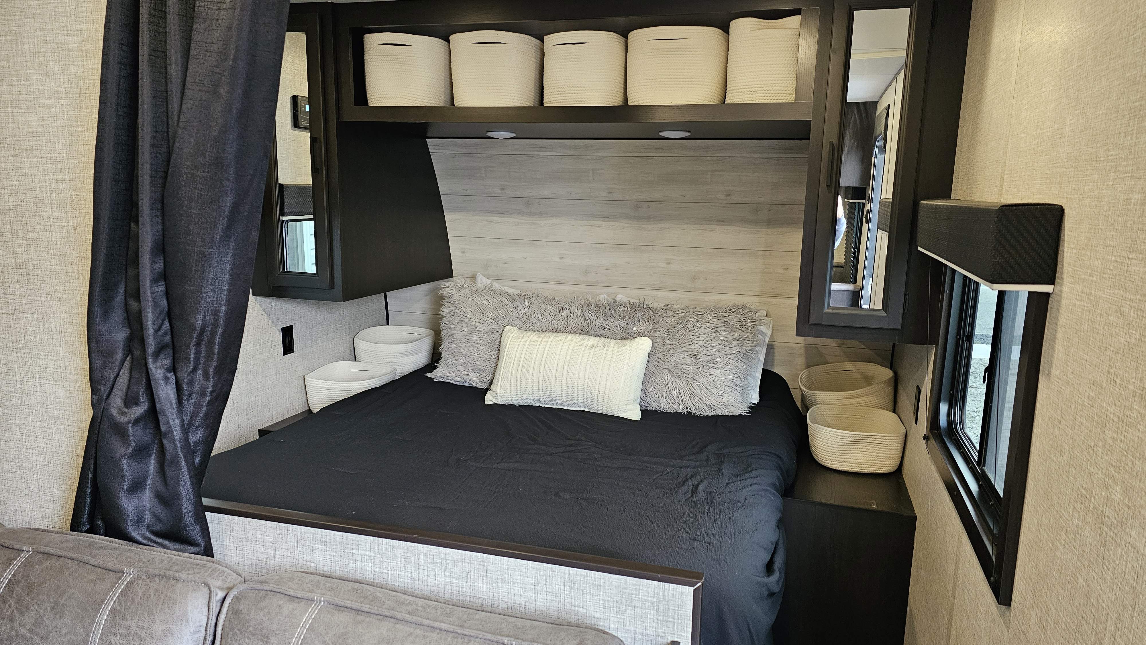 Inside an RV rental: a cozy bedroom with a dark bed, fluffy pillows, overhead baskets, & side window. Ideal for trips.. Jayco Jay Flight Baja Edition 2023