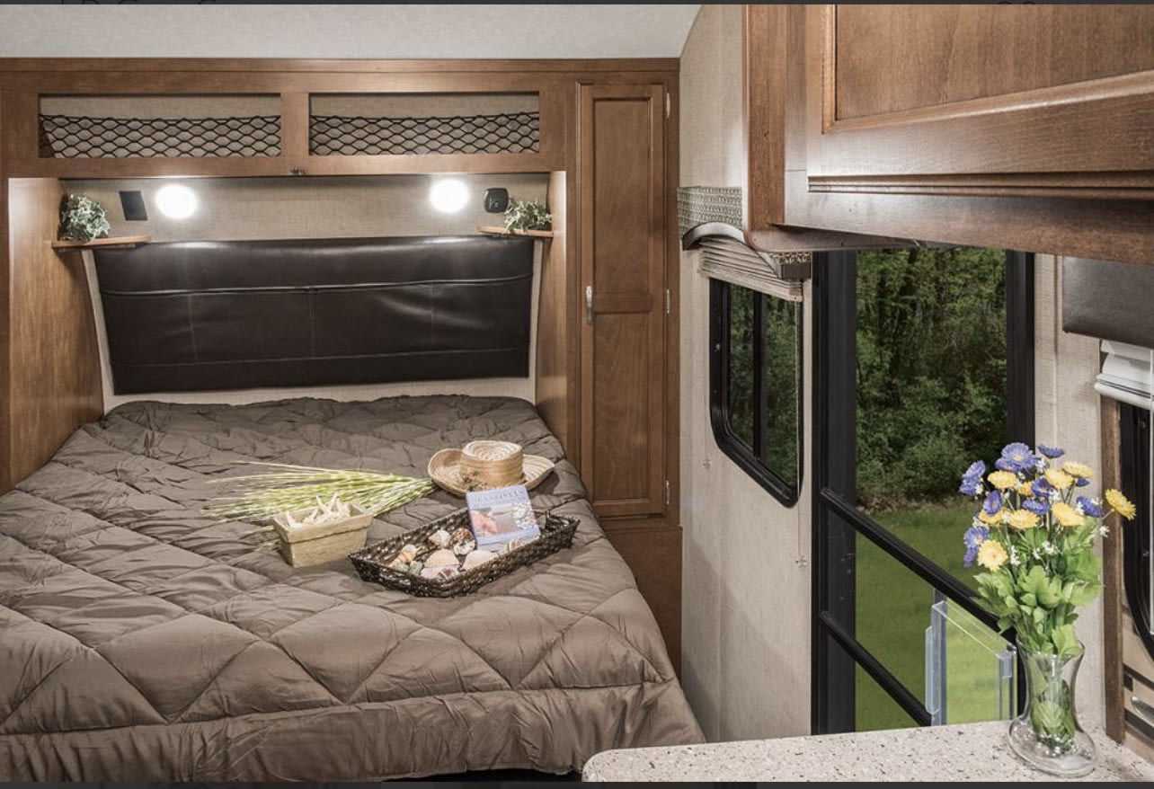Experience comfort in this RV rental bedroom: a cozy quilted bed, smart storage, and a window framing a lush outdoor view.. Sonic Lite 2017
