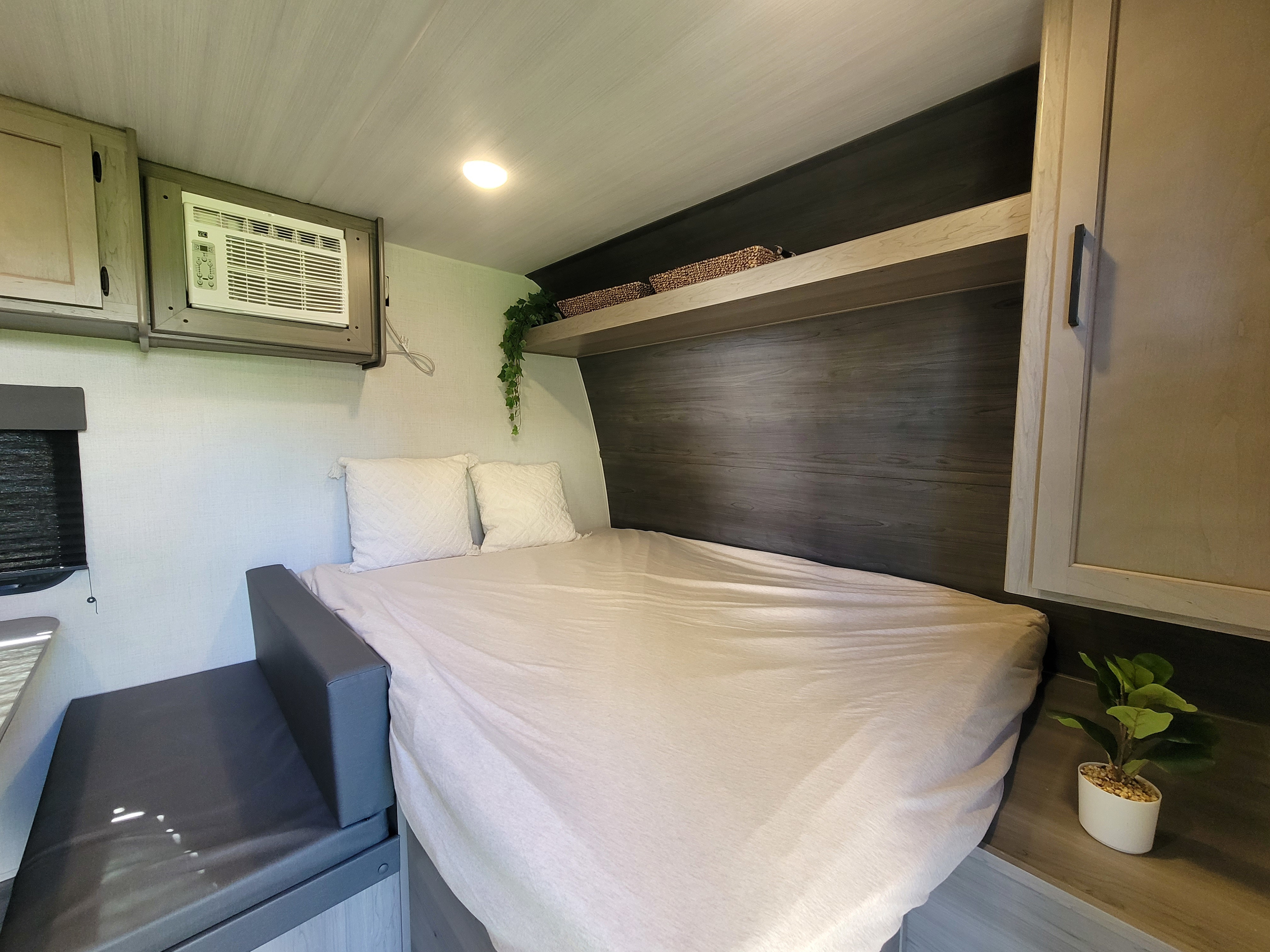 Cozy RV rental bedroom featuring a bed, AC unit, cabinets, and a side bench, ideal for a comfortable stay.. Keystone RV Hideout 2024
