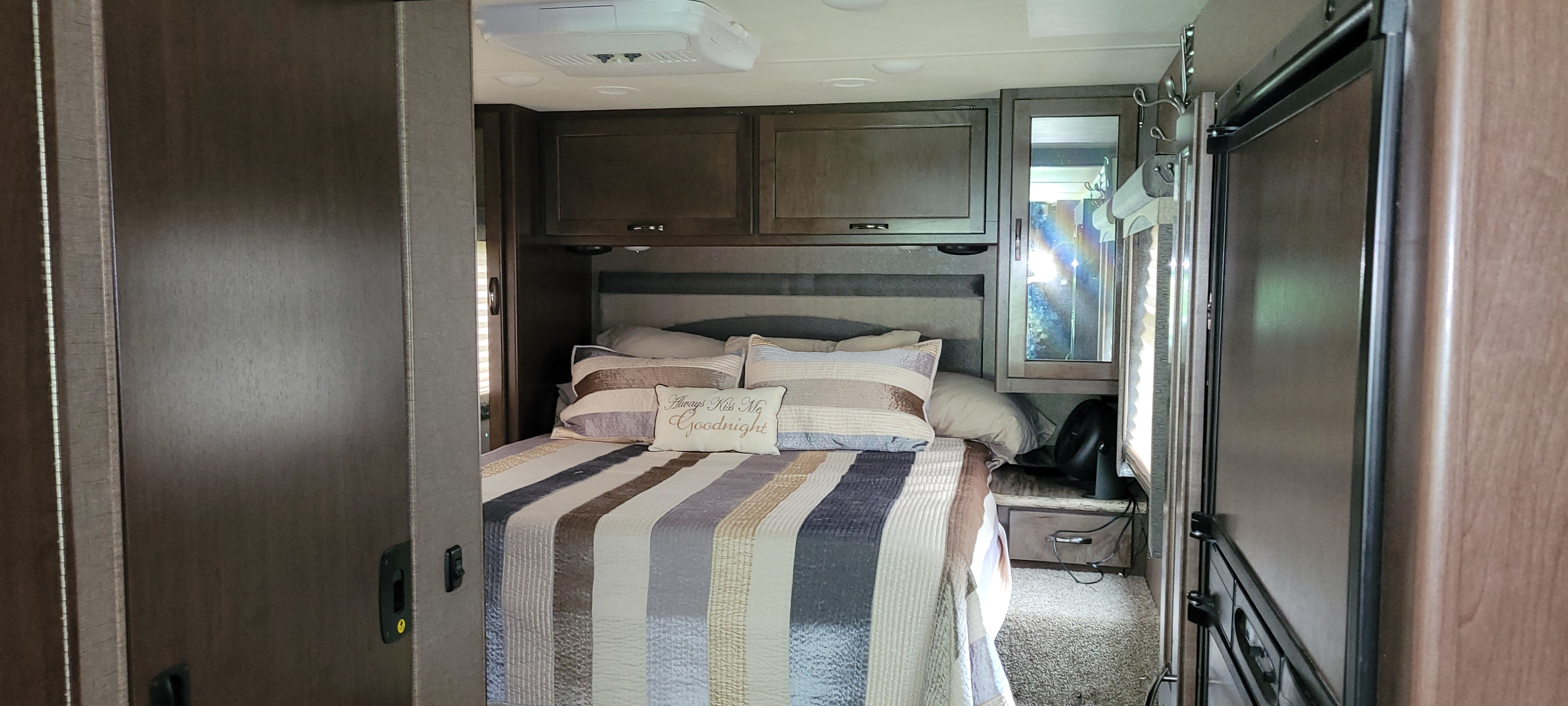 Cozy RV rental bedroom view: comfortable bed with striped comforter, overhead storage, ceiling AC, and a bedside fan.. Thor A.C.E. 2017