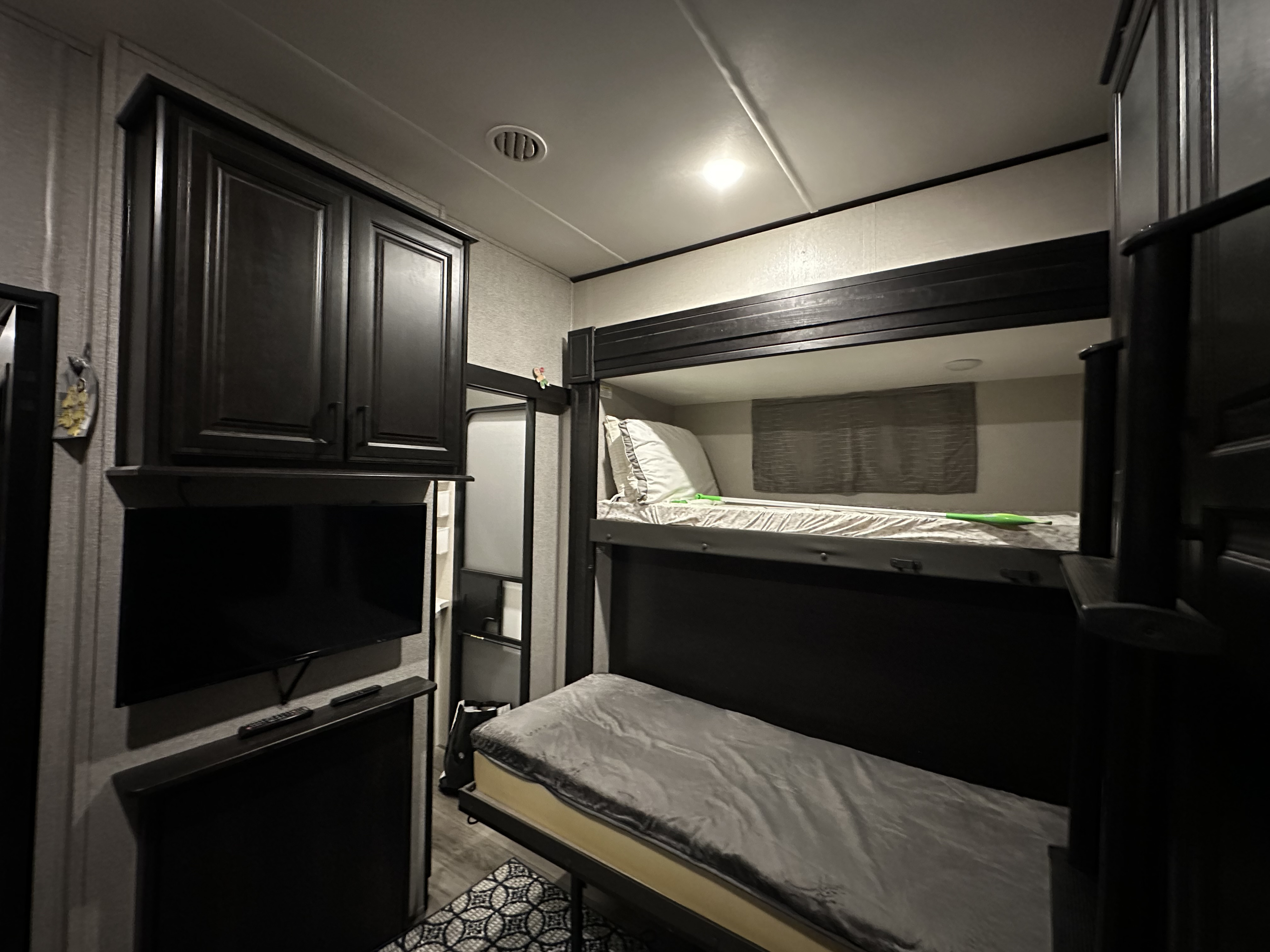 Interior of an RV rental: dark bunk beds, wall-mounted TV, and overhead cabinets create a compact, functional living space.. Highland Ridge RV Mesa Ridge XLT 2021