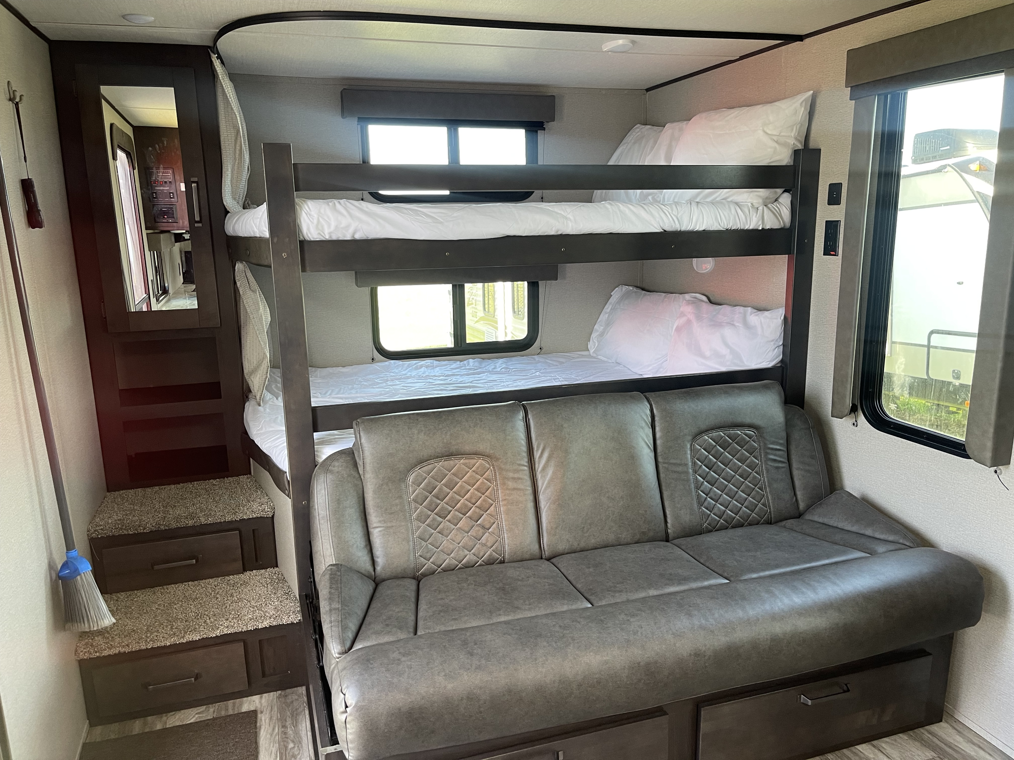 Bright RV rental interior features cozy bunk beds, a comfortable grey sofa, and storage steps for family adventures.. Grand Design Transcend Xplor 2022