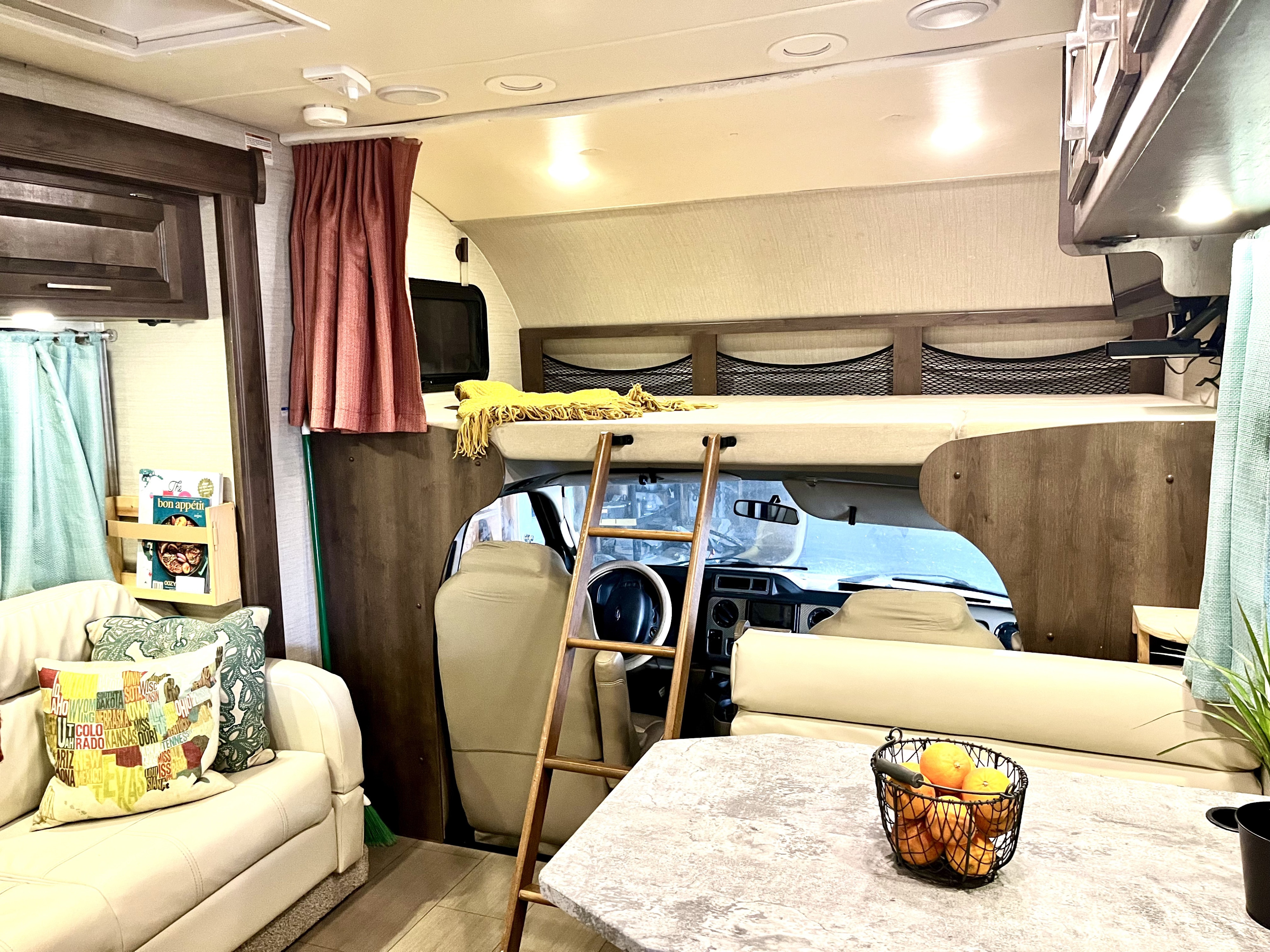 Inside a modern RV rental: comfortable living space, dining area, and a large bunk bed above the driver's cab.. Jayco Greyhawk 2018