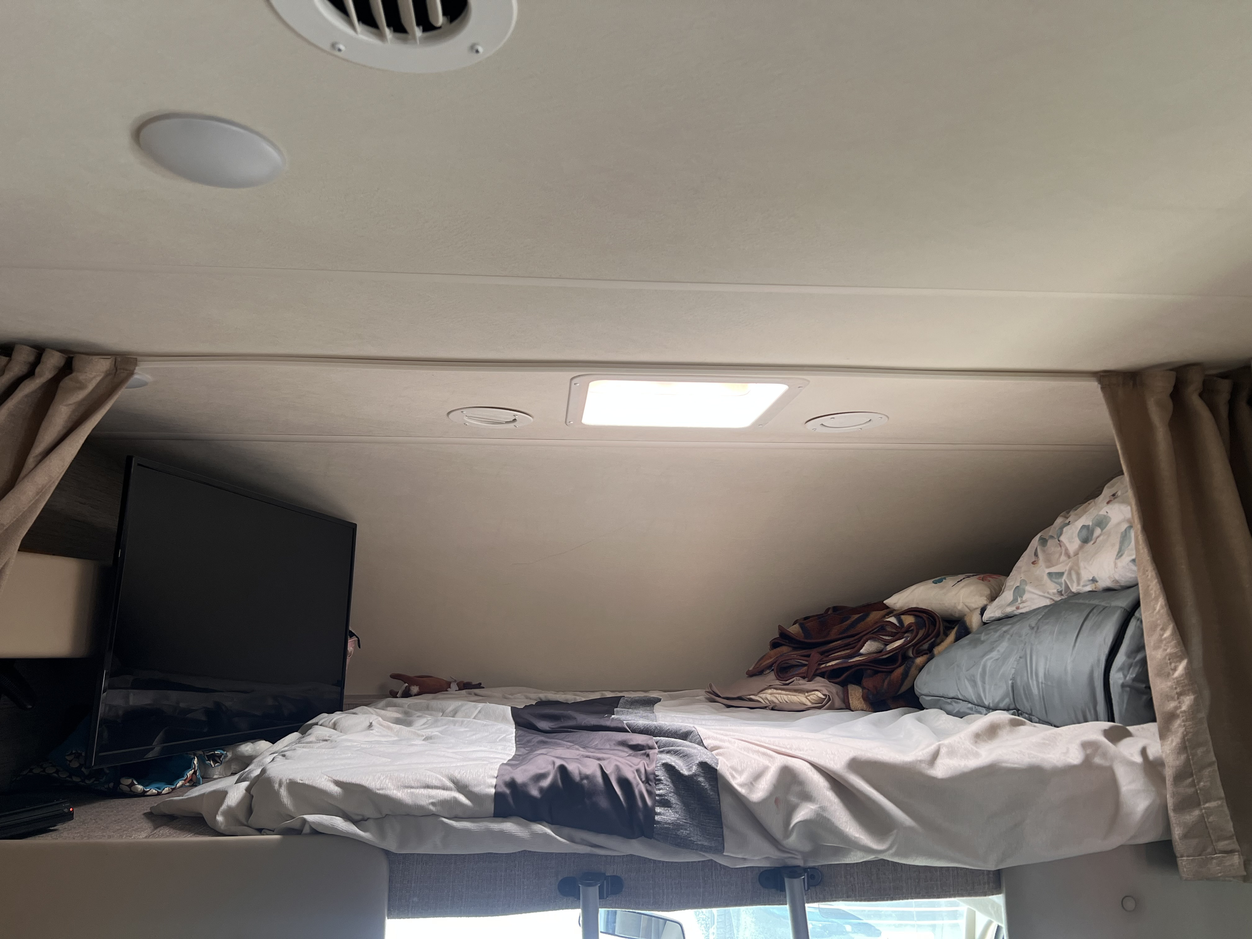 Overhead bunk sleeping area of an RV rental, complete with a TV, bed, and cozy bedding.. Thor Chateau 2022
