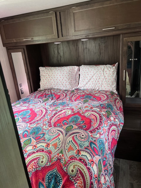 Step inside this cozy RV rental bedroom featuring a vibrant paisley comforter, overhead storage, and mirrored closets.. Forest River Cherokee 2019