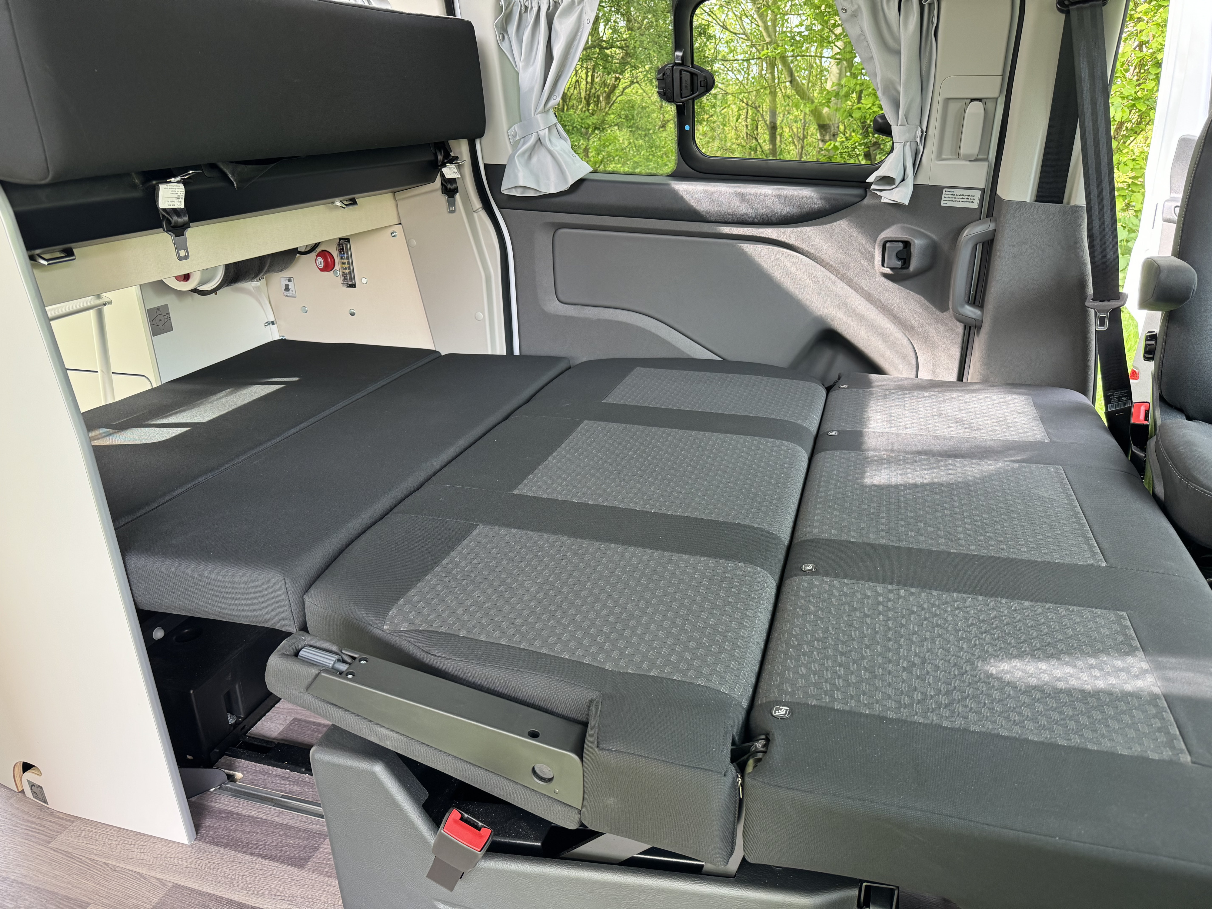 Inside an RV rental: rear seats fold down to a bed. Features windows with curtains, safety belts, and storage.. Ford Nugget 2022