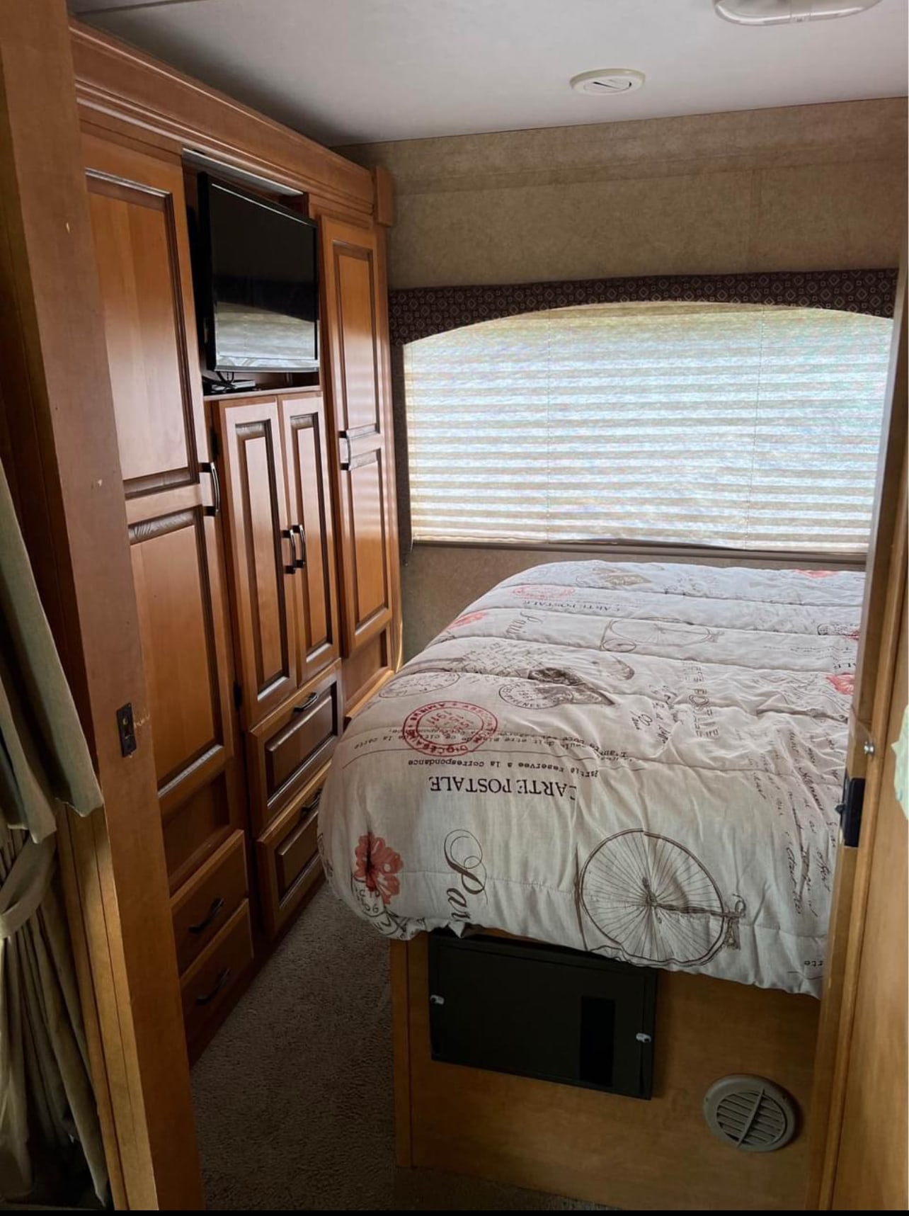 This RV rental bedroom offers compact comfort with a postcard-themed bed, built-in TV, window blinds, and wood cabinetry.. Forest River Sunseeker 2011