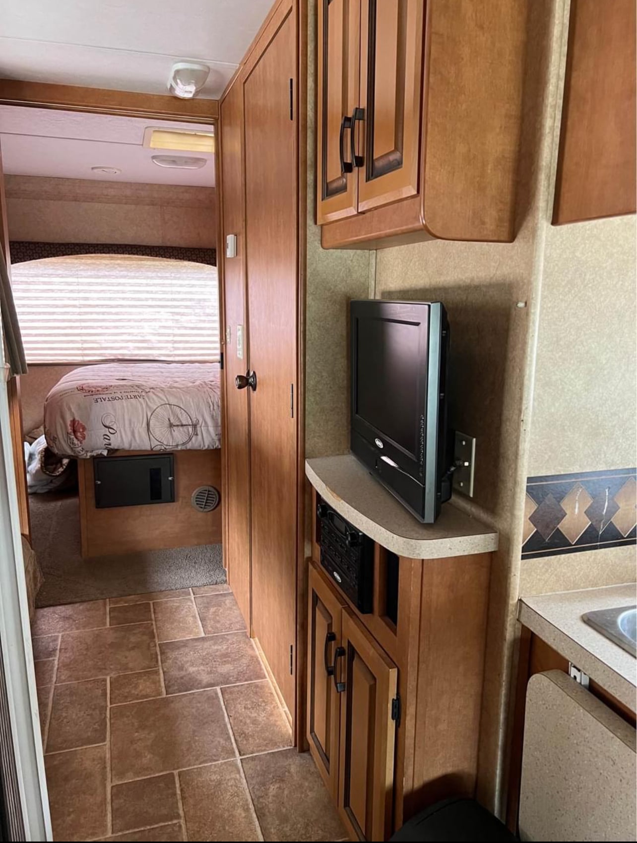 RV rental interior: bedroom with bed & window, entertainment center with TV, and wood cabinets. Clean, functional travel space.. Forest River Sunseeker 2011