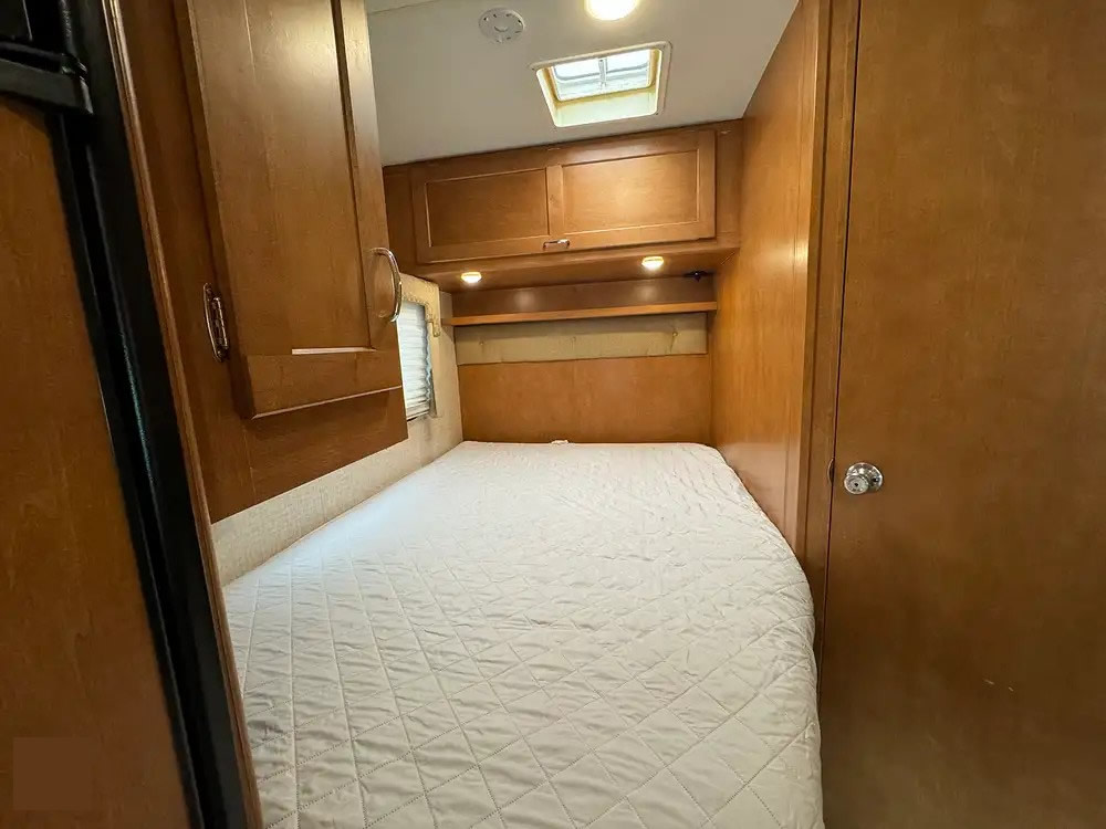 RV rental interior: A cozy bedroom featuring a white quilted bed, wood cabinetry, overhead storage, and a skylight.. Winnebago Minnie Winnie 2017