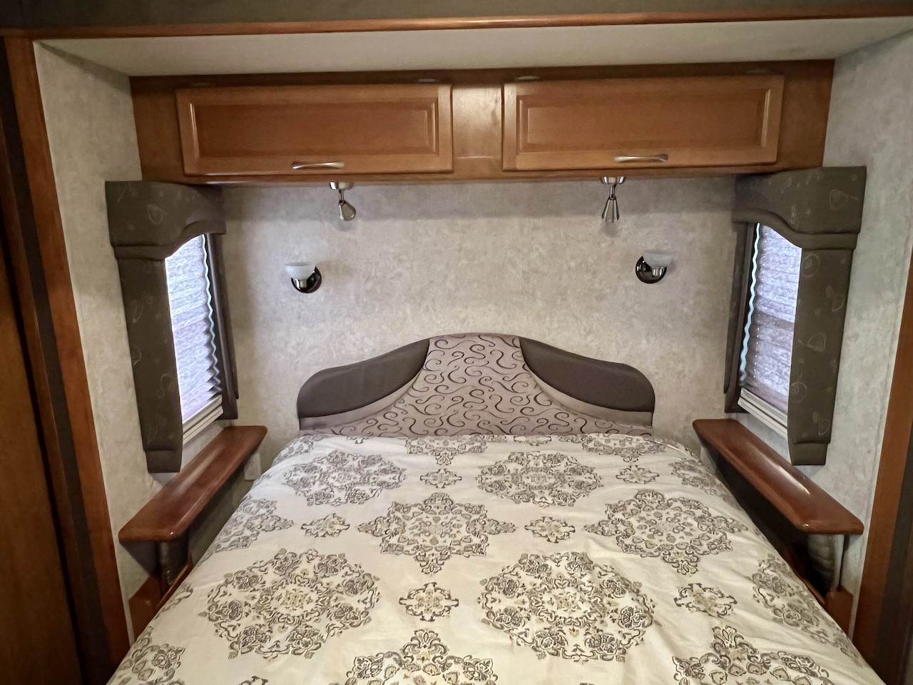 Cozy RV rental bedroom featuring a patterned bed, overhead cabinets, reading lights, and side windows for a comfortable journey.. Fleetwood Pace Arrow 2004