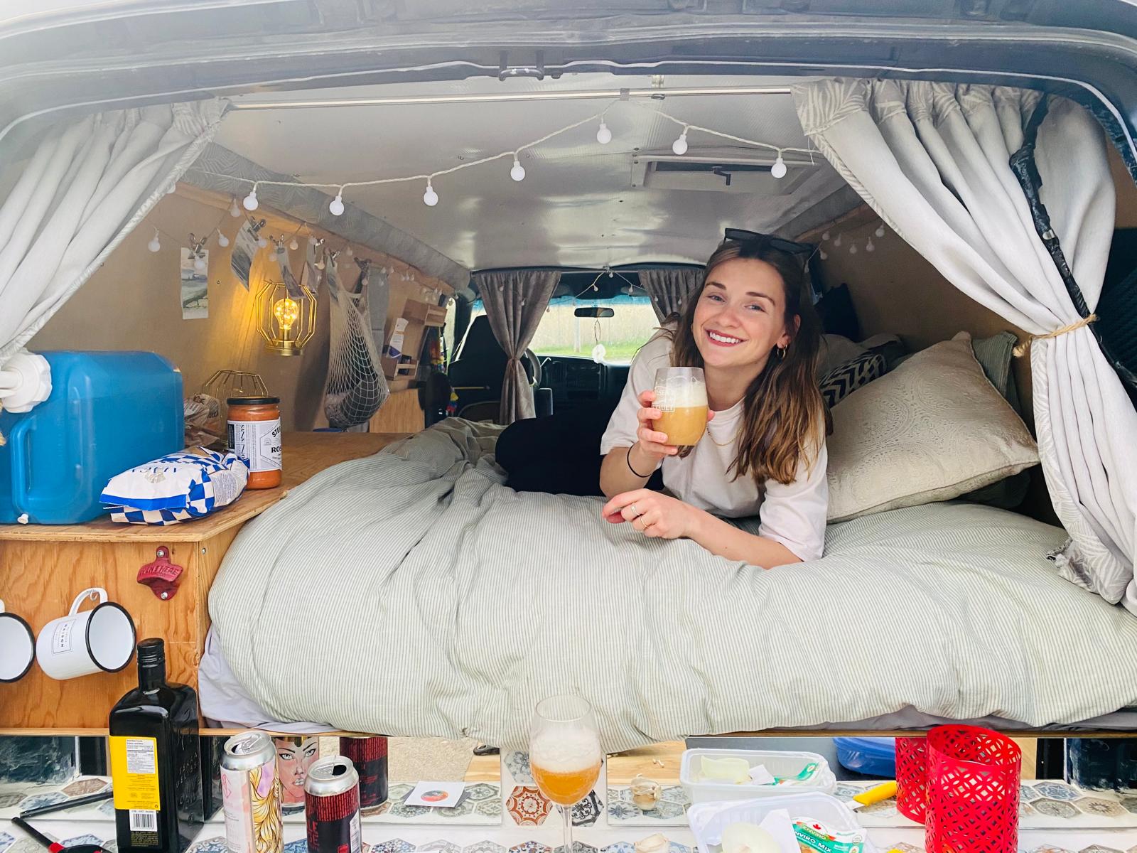 Smiling woman unwinds on a comfy bed in her converted **RV rental**. Cozy van life setup with essentials for travel adventures.. Chevrolet Express 2001