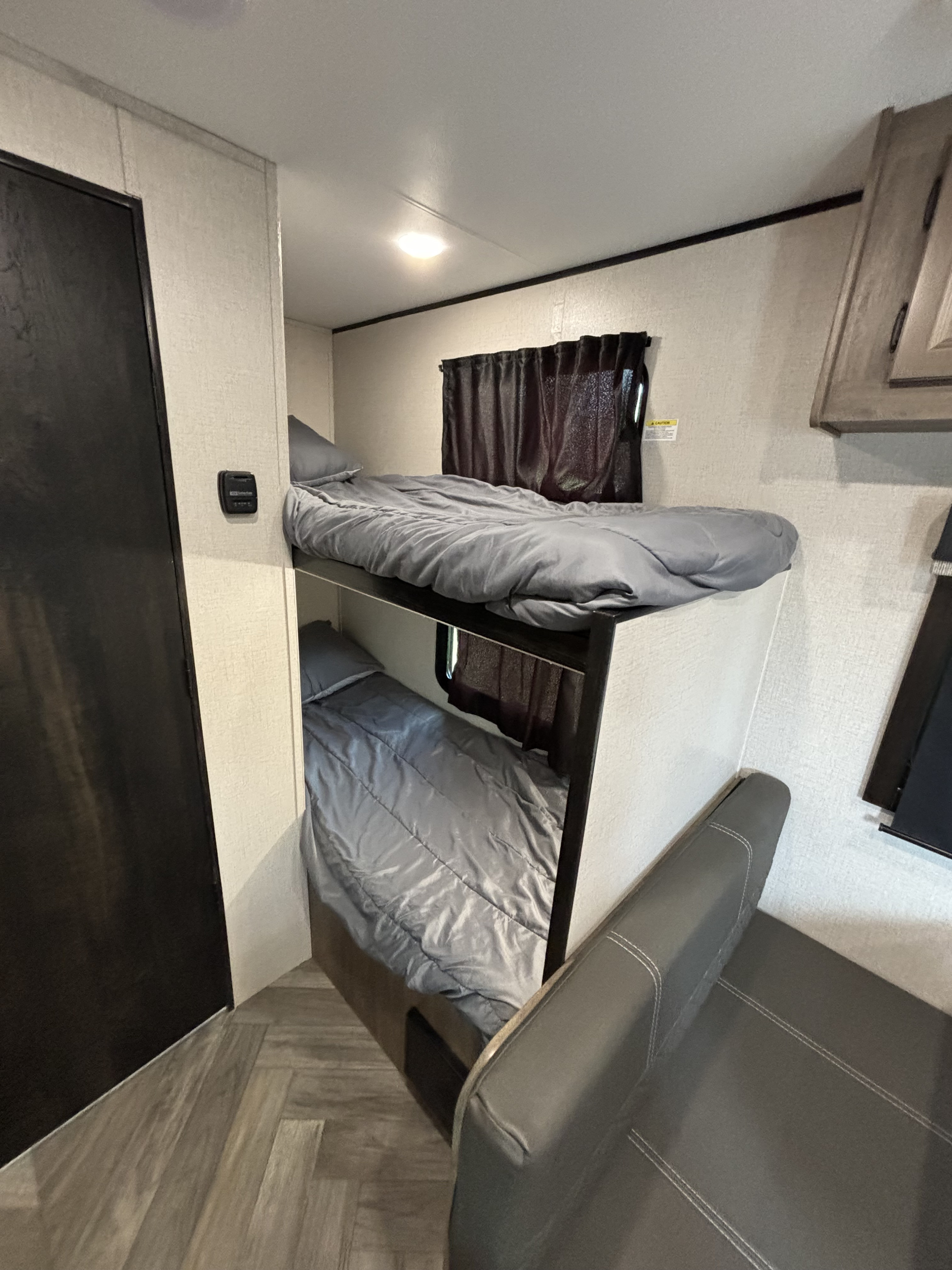 This RV rental's sleeping area features two compact bunk beds with grey bedding, dark curtains, and a seating area.. Olympia Sport 19BH 2022