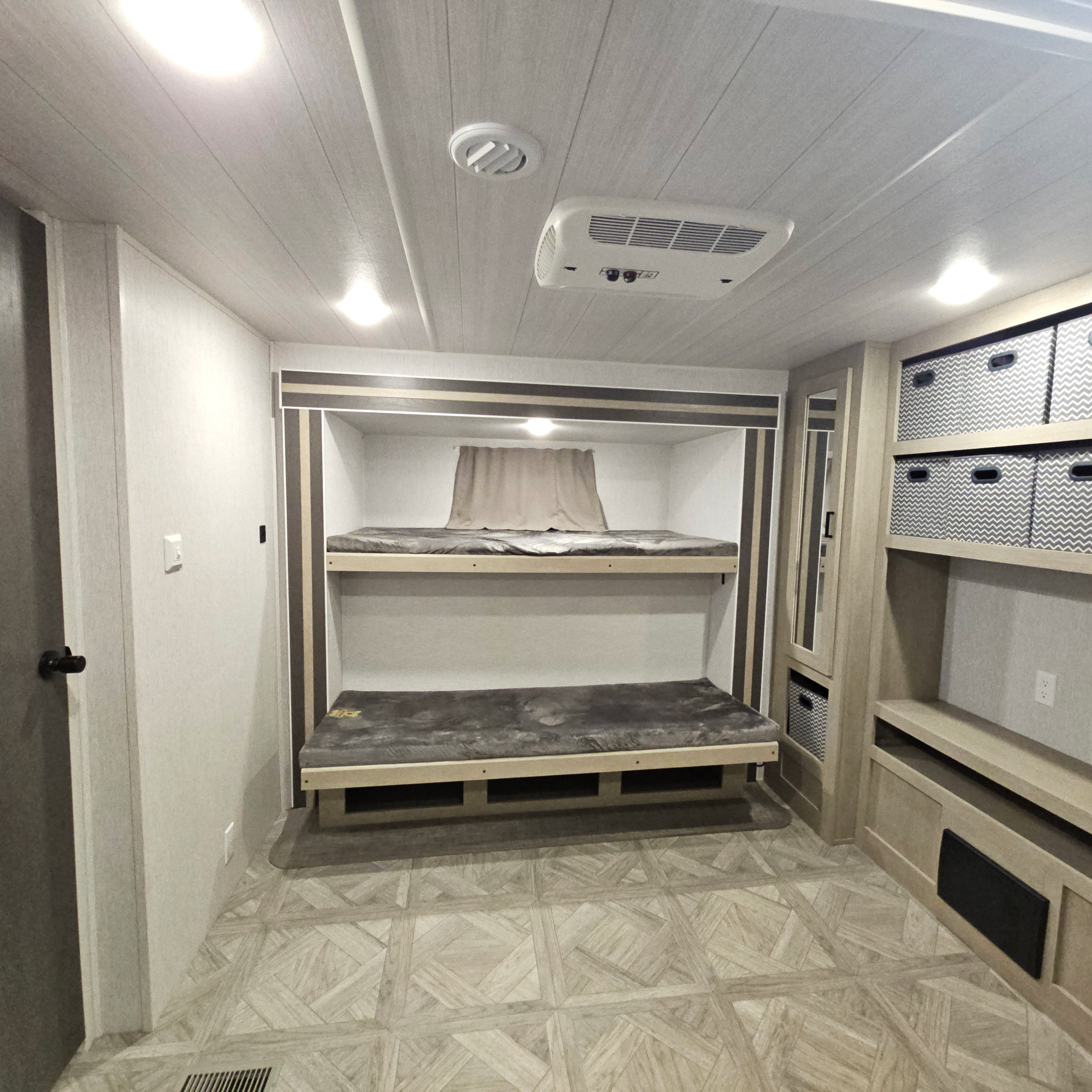 Interior of an RV rental: cozy bunk beds, ample storage with chevron bins, and a light, modern design.. Forest River Salem Platinum 2023