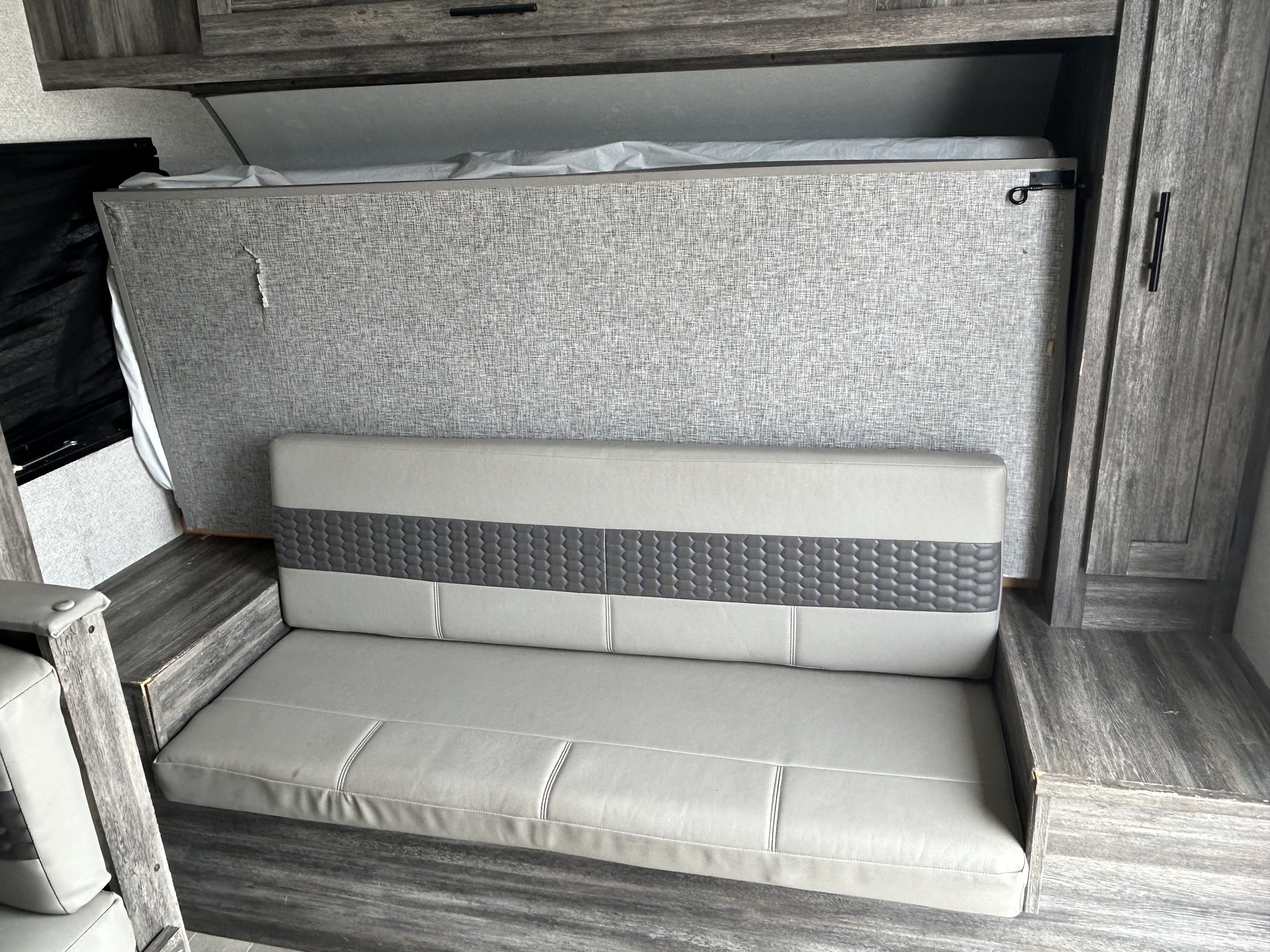 RV rental interior showing a space-saving murphy bed folded above a comfortable gray sofa, maximizing camper living.. Forest River Wildwood 2021