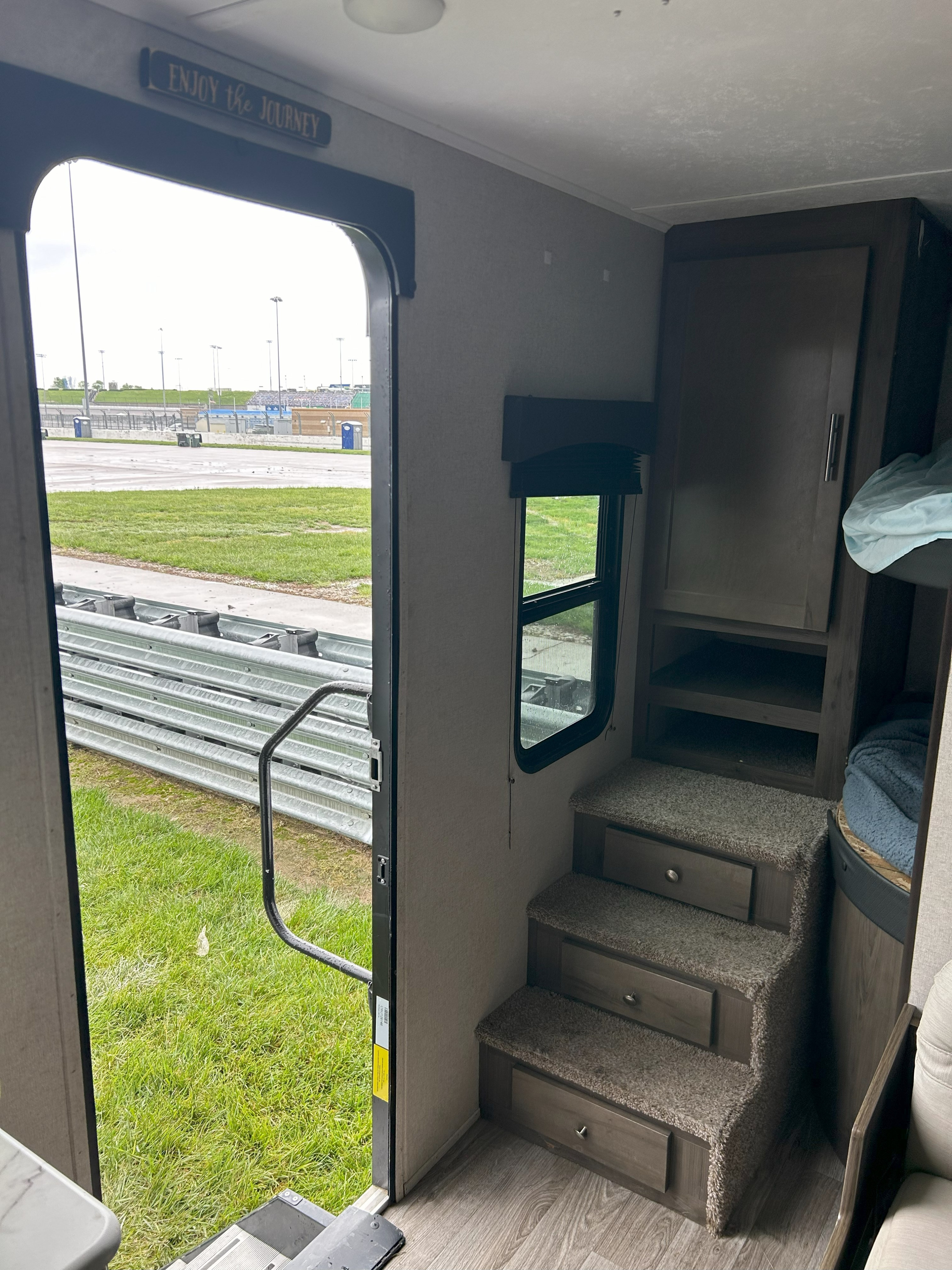 RV rental interior: steps, storage, bunk, and an open door viewing a race track, grass, and guardrails outside.. Coachmen Clipper 2021