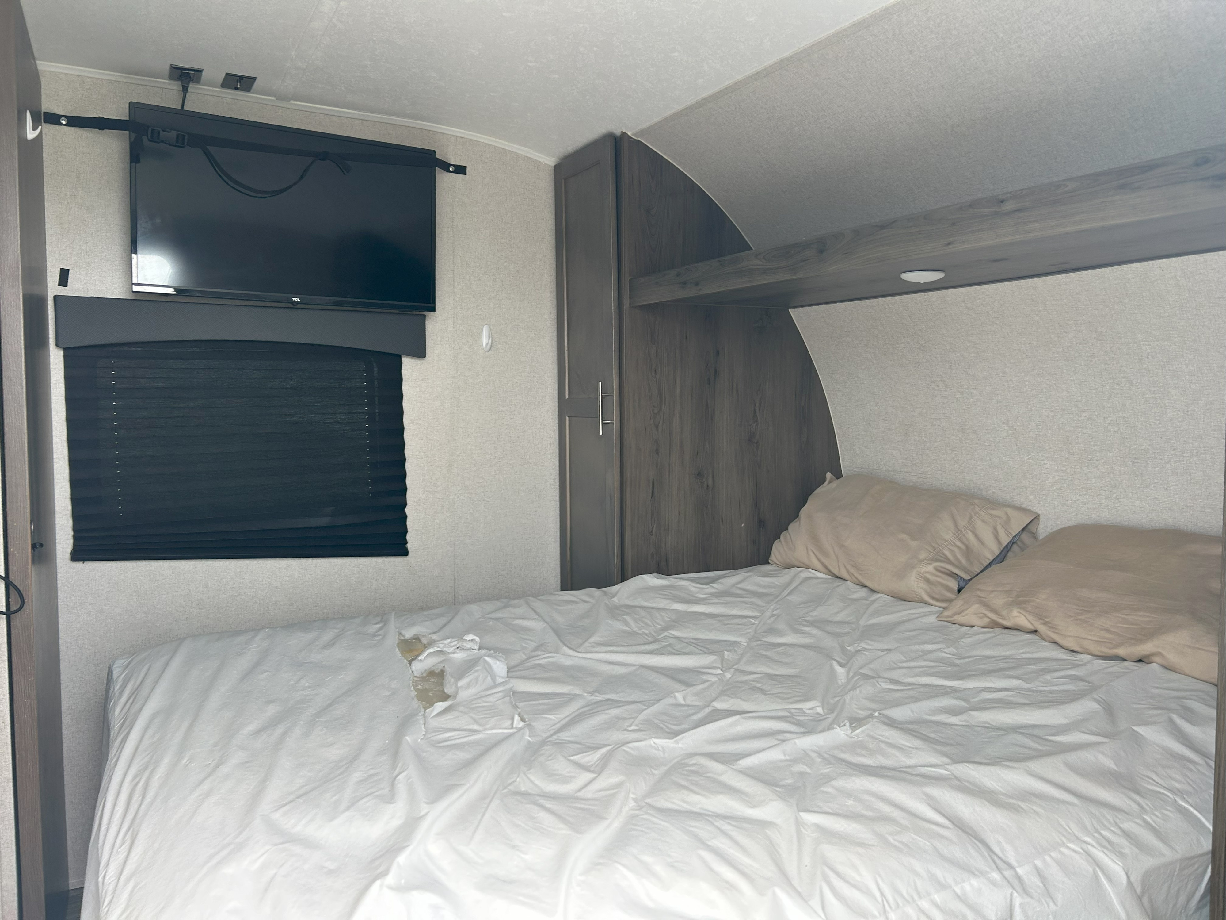 Inside an RV rental bedroom: a bed with torn white sheets, TV, and built-in storage. A compact and functional space.. Coachmen Clipper 2021