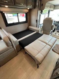 Inside an RV rental, a light-colored sofa converts into a bed with a black mattress, offering flexible sleeping in the living area.. Entegra Coach Vision XL 2023