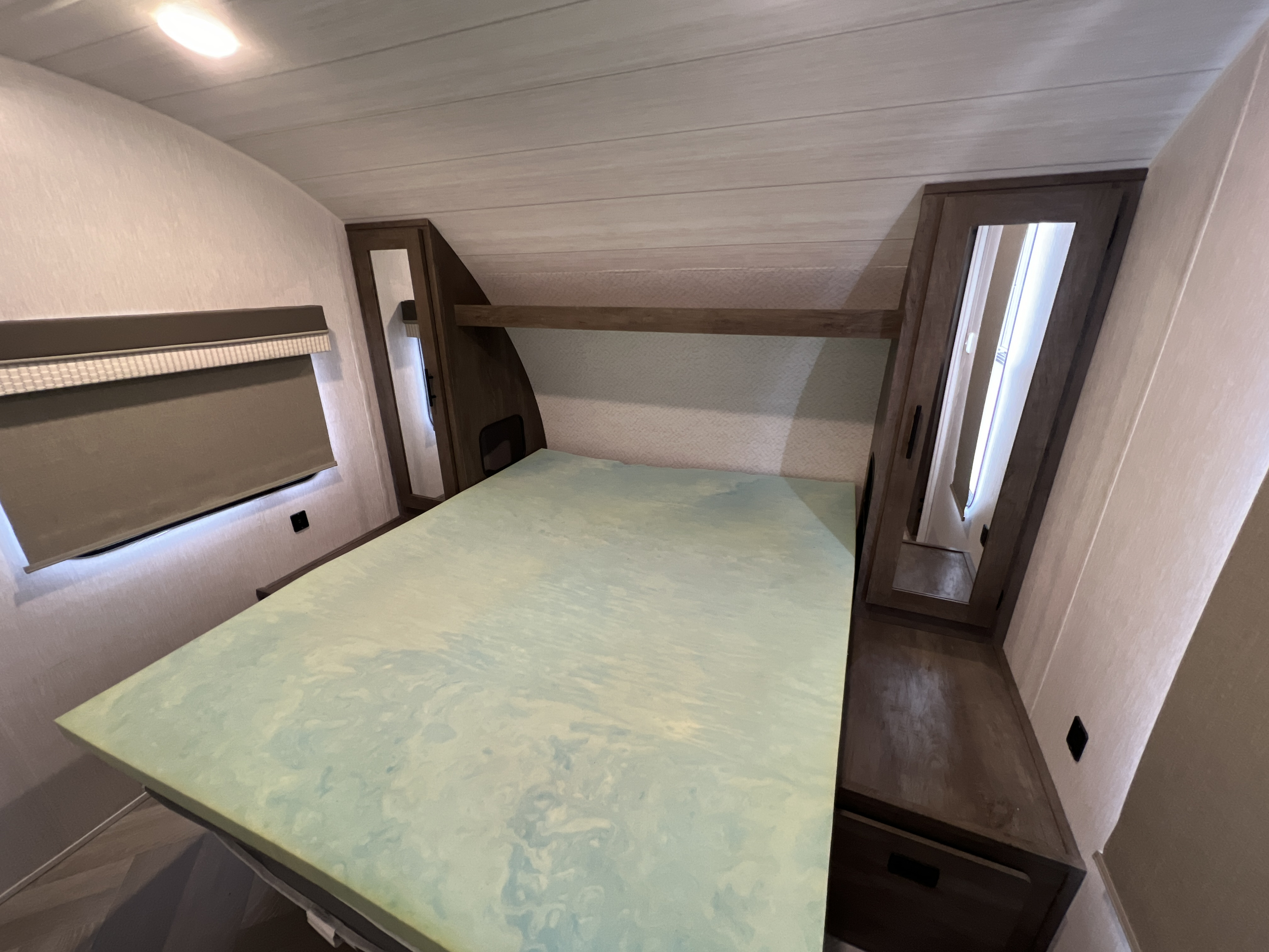 RV rental bedroom: a cozy space featuring a bed with a light green swirled topper, window, and built-in wood cabinets.. Forest River Wildwood X-Lite 2022
