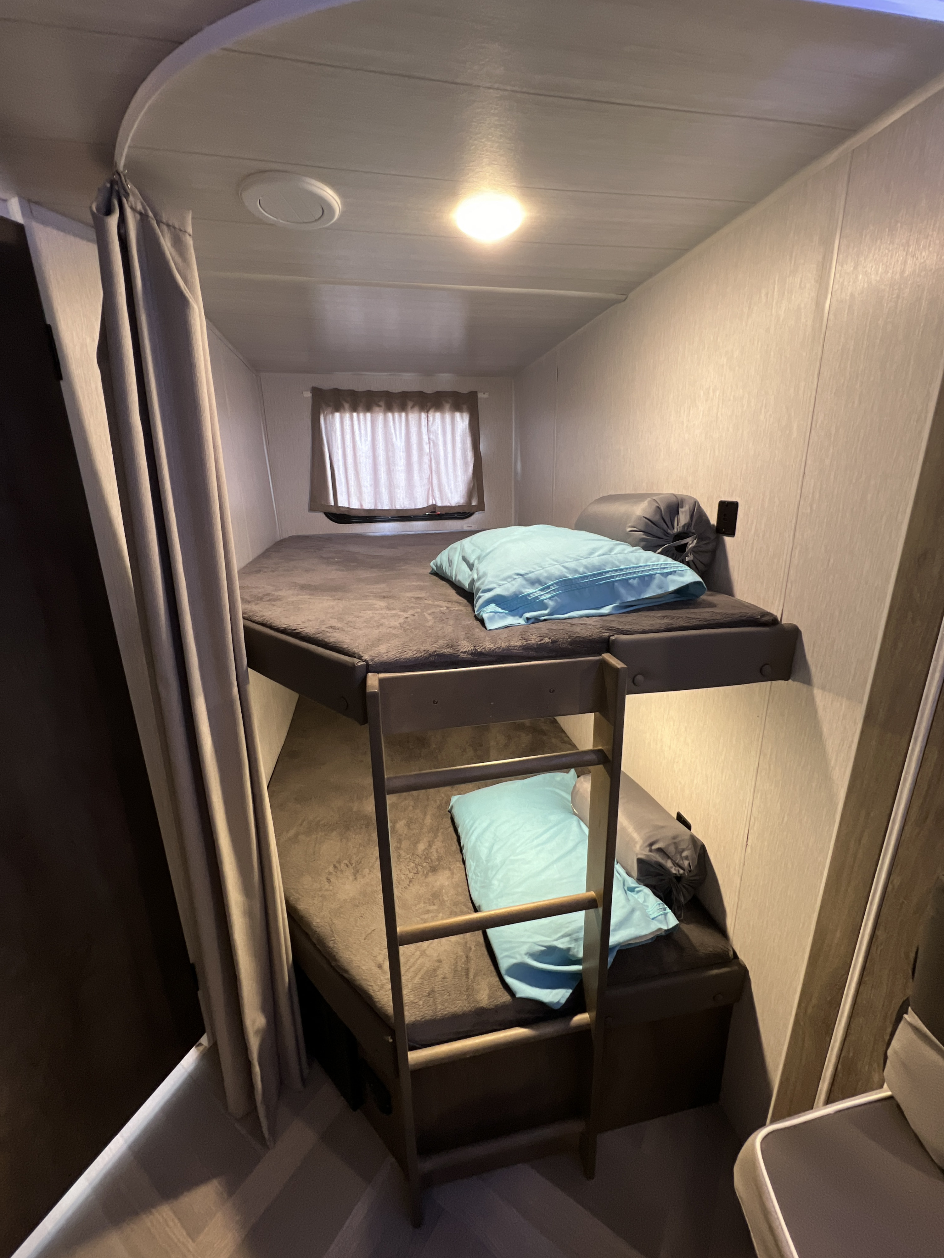 Cozy bunk beds in an RV rental, featuring soft mattresses, blue pillows, a ladder, and a privacy curtain.. Forest River Wildwood X-Lite 2022