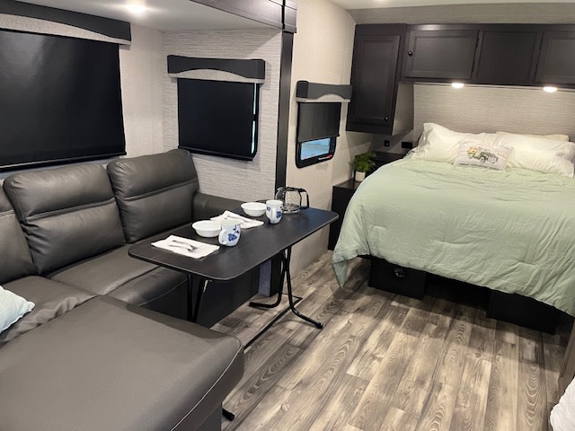 Inside an RV rental: a modern, compact space with dark gray sectional sofa, dining table, and bed with light green bedding. Ready for travel.. Highland Mesa Ridge S Lite 2022