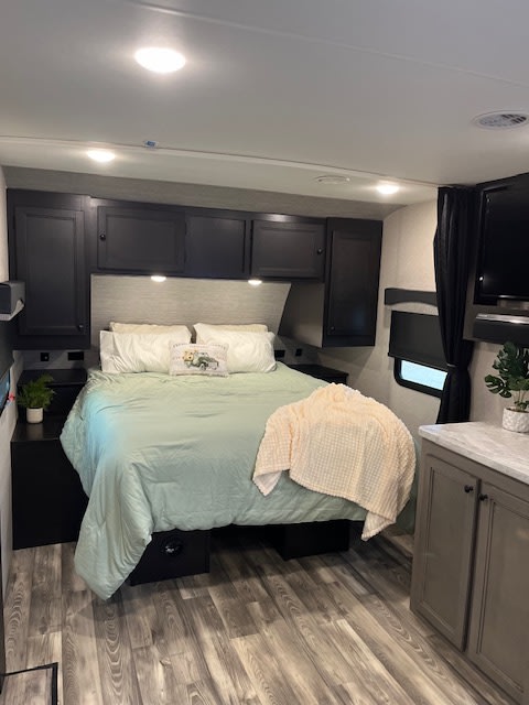 Cozy RV rental bedroom featuring a queen bed, dark cabinets, and wood-look flooring. Ready for your adventure.. Highland Mesa Ridge S Lite 2022
