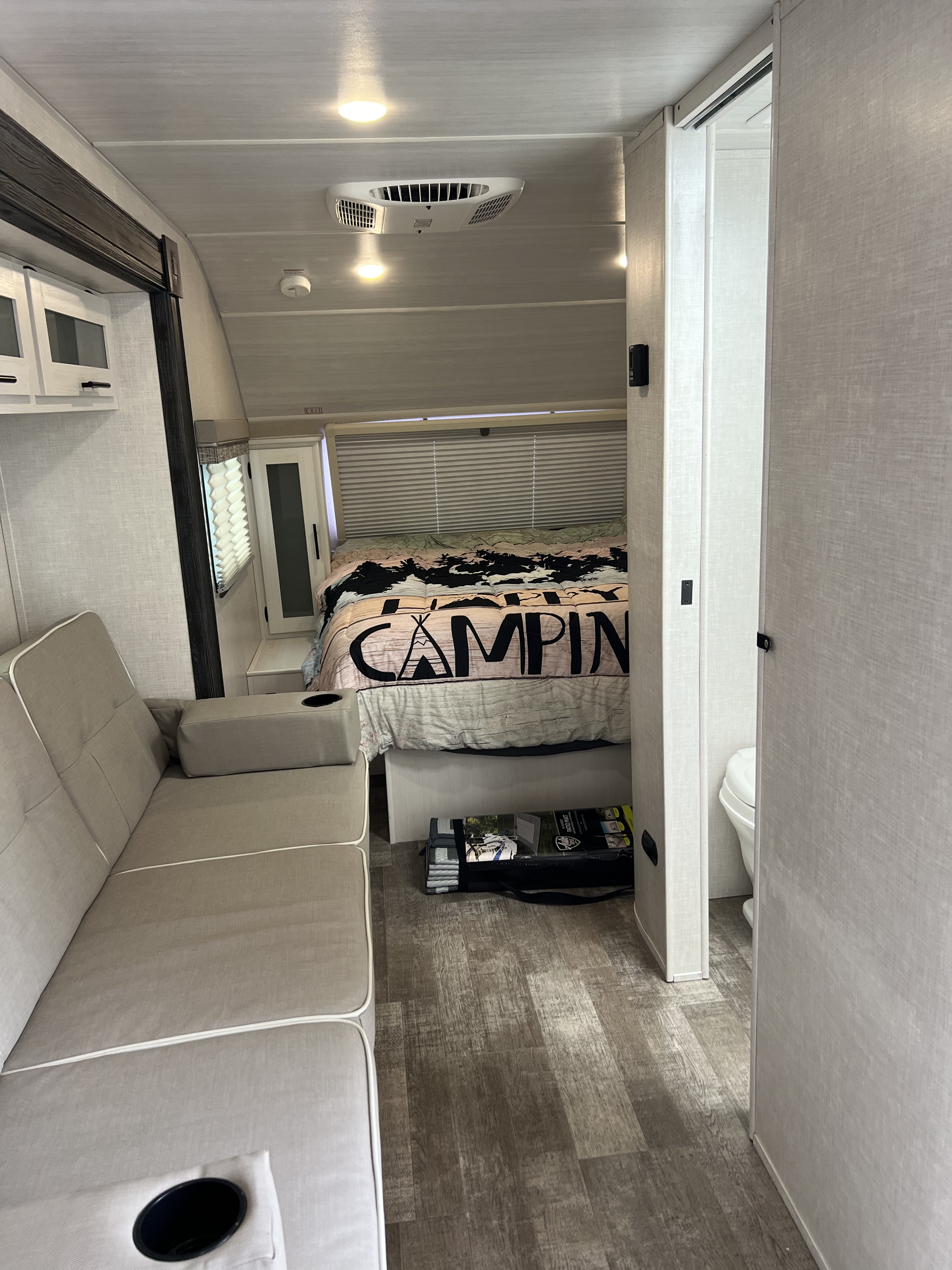 Inside this rv rental, a compact bedroom with a "CAMPING" bed, comfy couch, and bathroom offer a cozy travel experience.. Forest River R -Pod 2022
