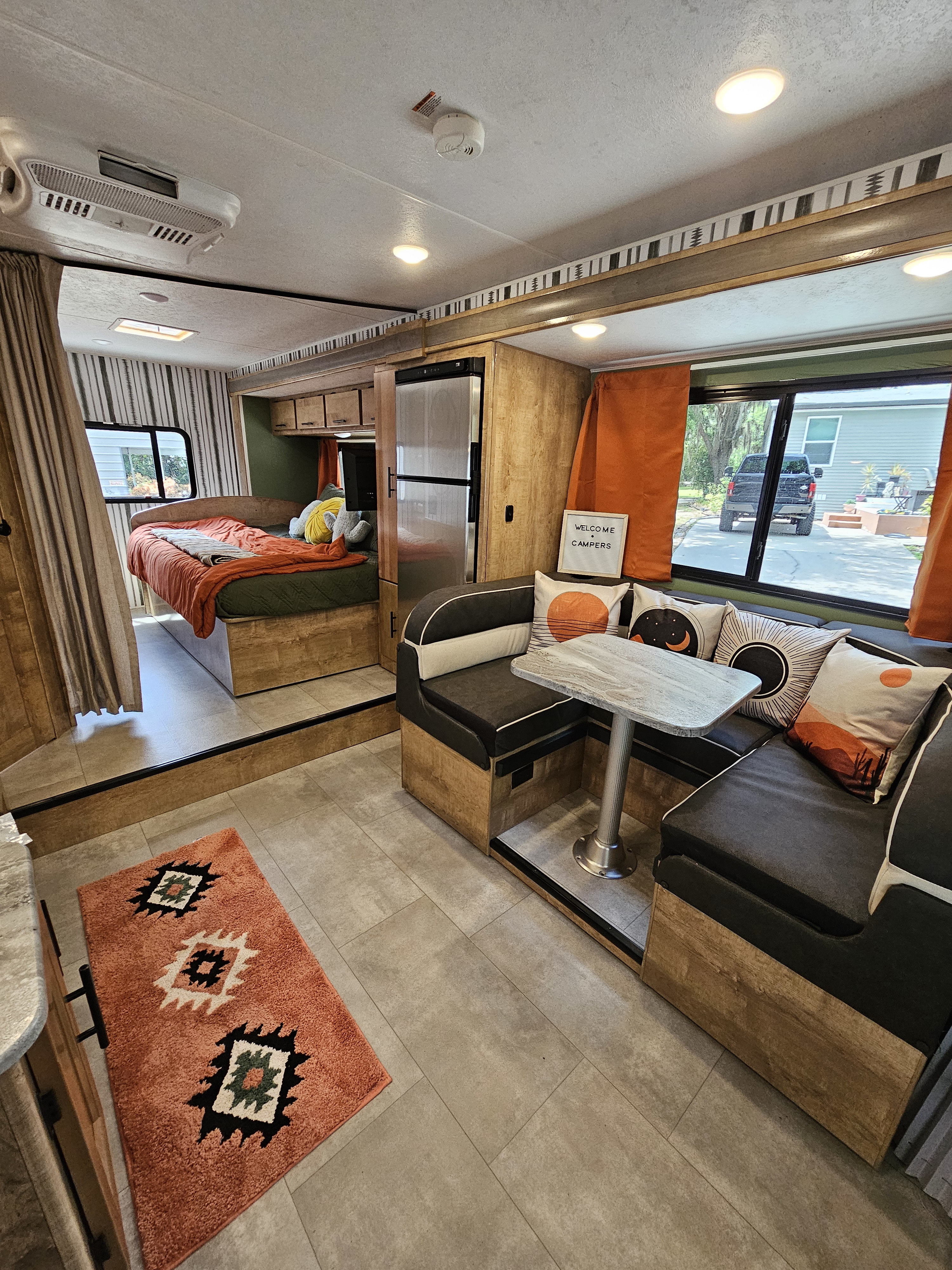Inside a vibrant rv rental: comfortable bedroom with orange bedding, dinette, and fridge.. Coachmen Leprechaun 2021