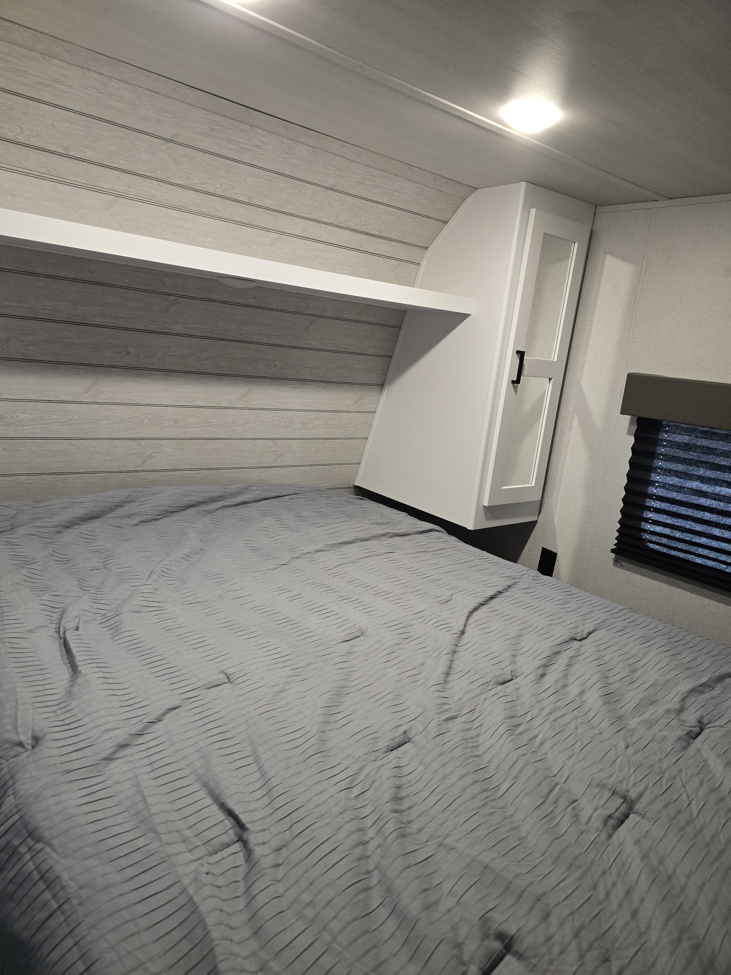 This modern RV rental bedroom features a comfy grey bed, white built-in storage, and light shiplap walls. Ideal for travel.. Keystone RV Hideout 2023