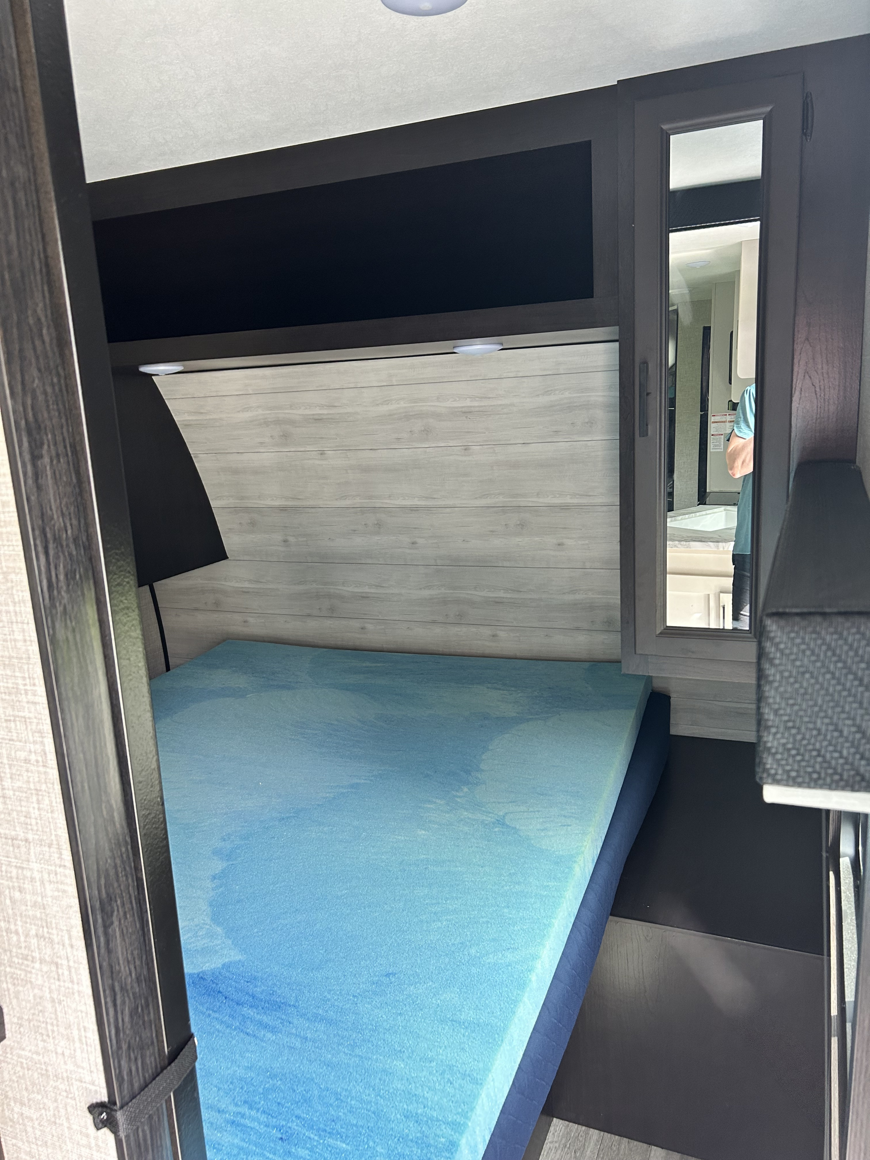 Inside an RV rental: a compact bedroom featuring a blue mattress, light wood-paneled wall, and a mirrored cabinet.. Jayco Jay Flight 2023