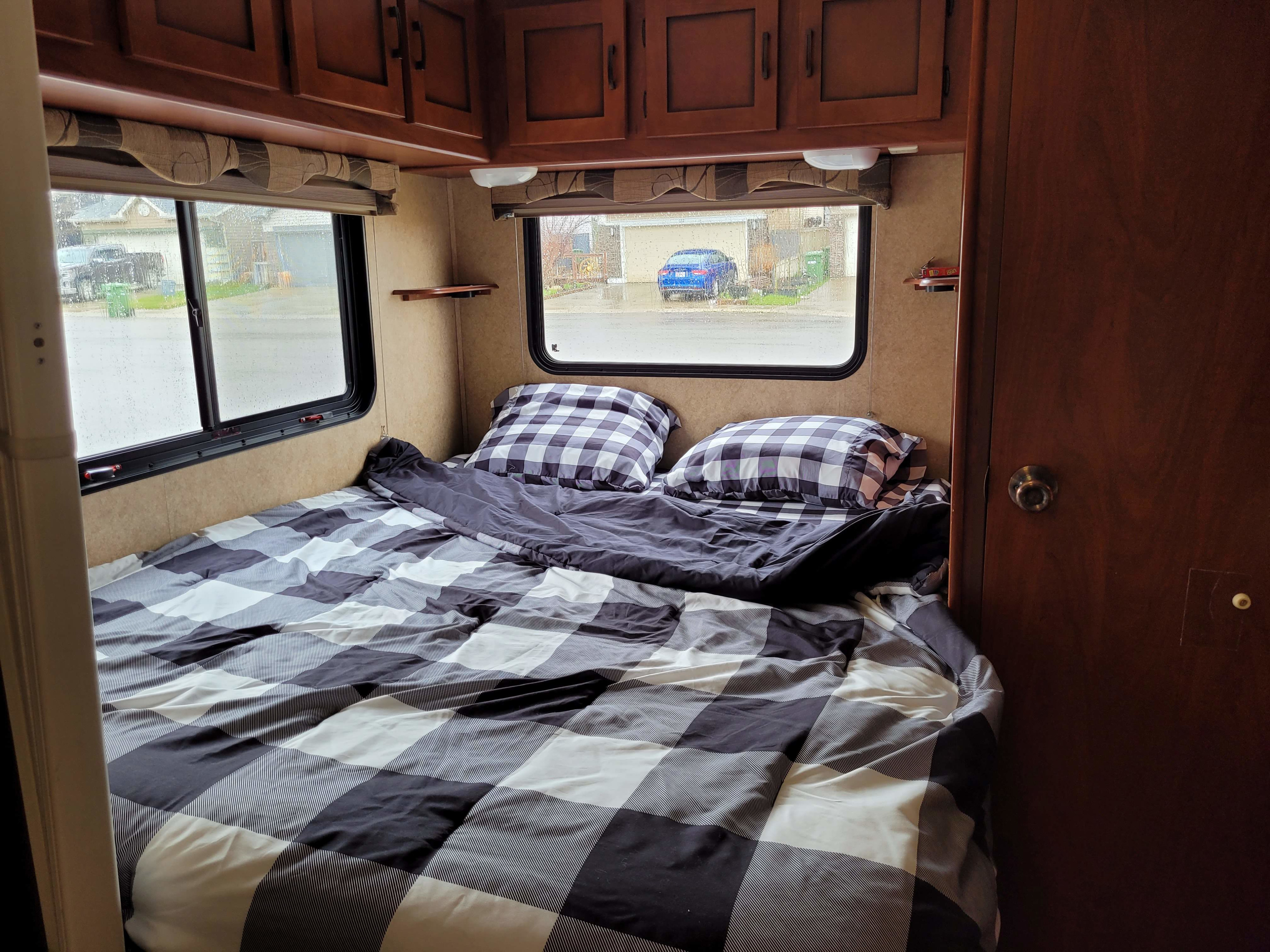 A comfortable RV rental bedroom with black and white checkered bedding, overhead cabinets, and a view through rainy windows.. Forester Forester Motorhome 2011