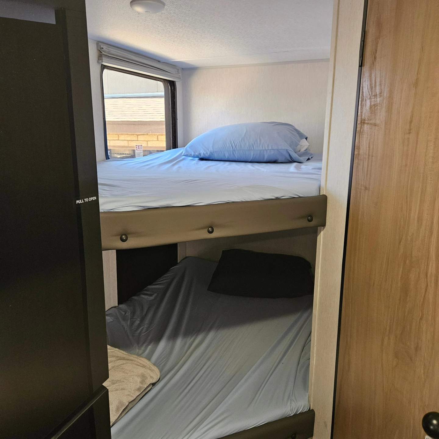 View of an RV rental's compact interior: two bunk beds with light blue sheets, pillows, a window on the top, and adjacent doors.. Forest River Cherokee Wolf Pup 17JW 2024