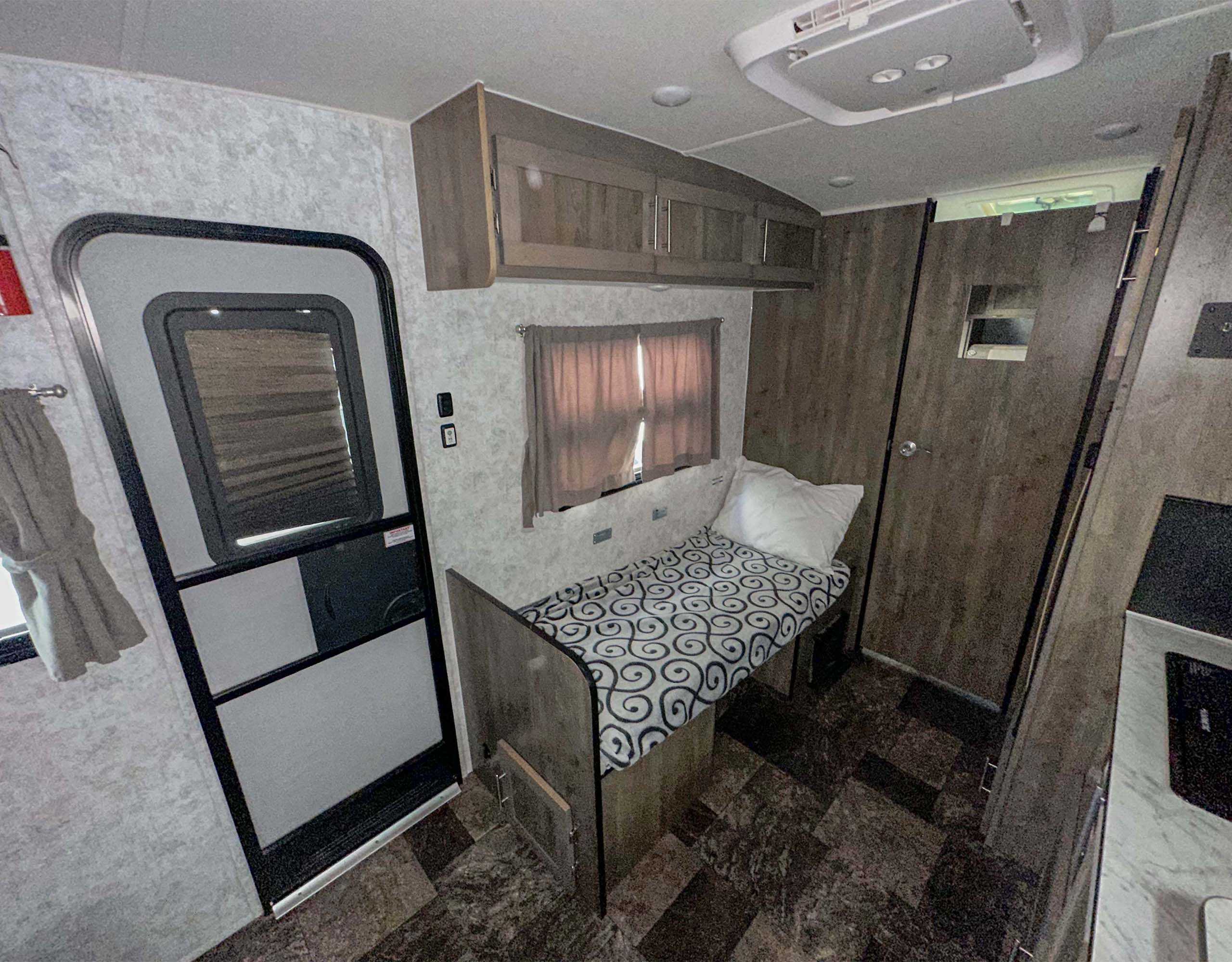 Compact RV rental interior with bench bed, overhead cabinets, and exit door. Cozy living space for travel.. Prolite Classic 2022