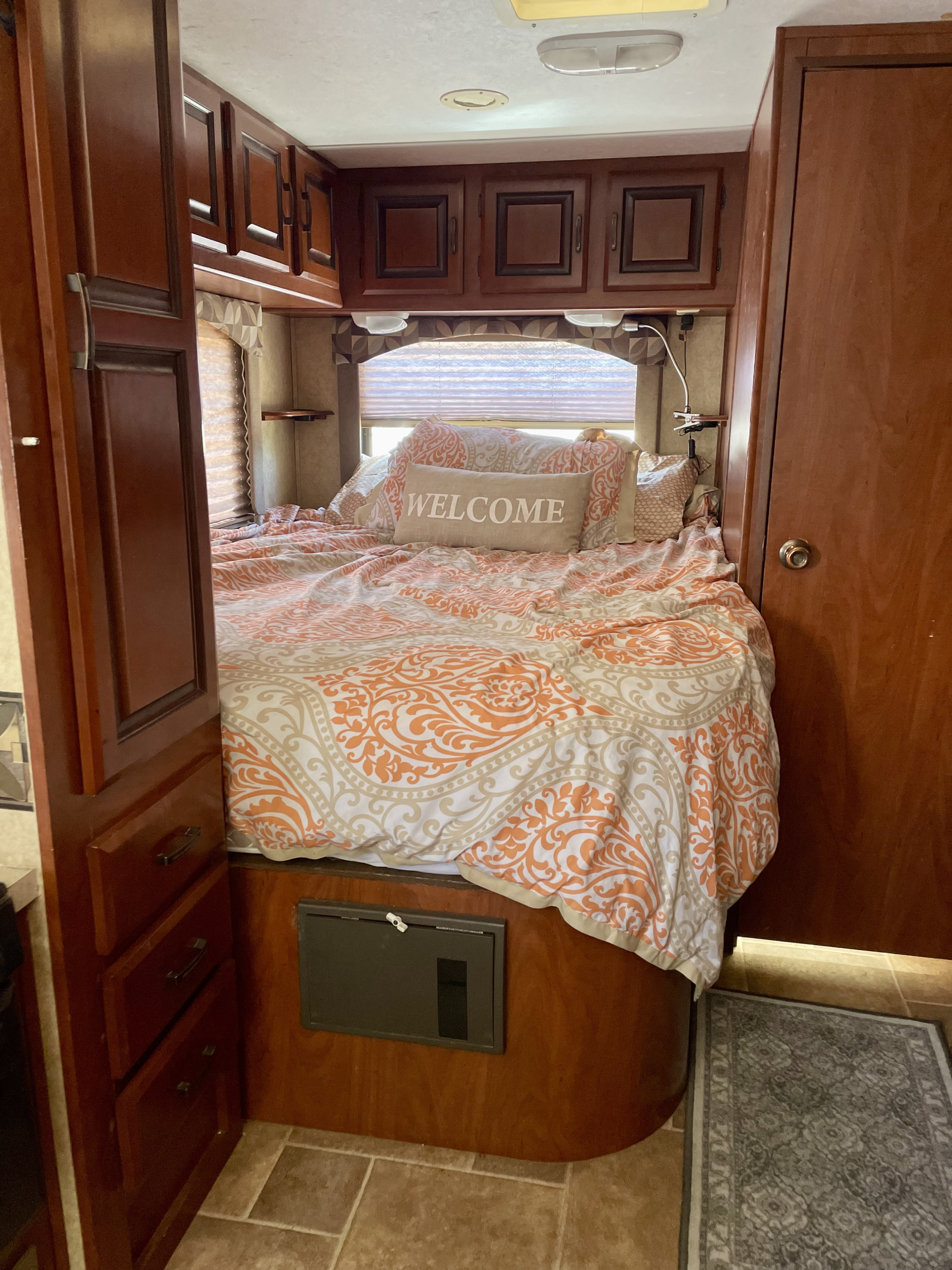 Relaxing RV rental bedroom featuring an orange and white patterned bed, wood cabinetry, and window nook.. Forest River Sunseeker 2012