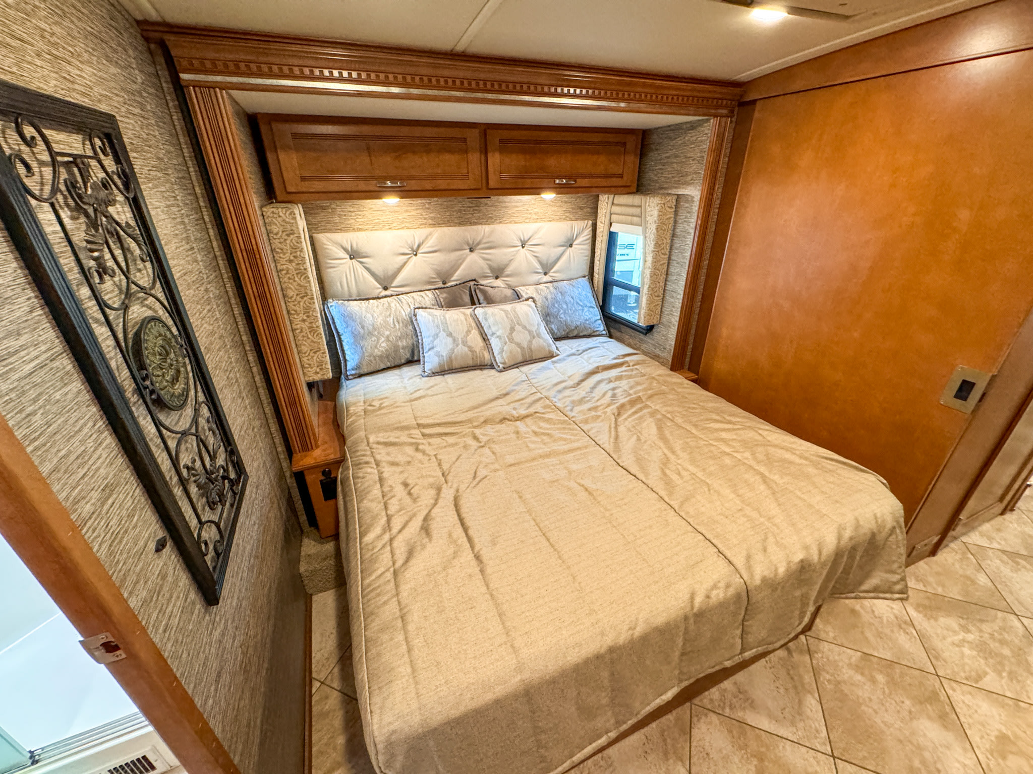 Cozy RV rental bedroom featuring a large bed, tufted headboard, and overhead storage. Ready for comfortable travel.. Winnebago Forza 2019