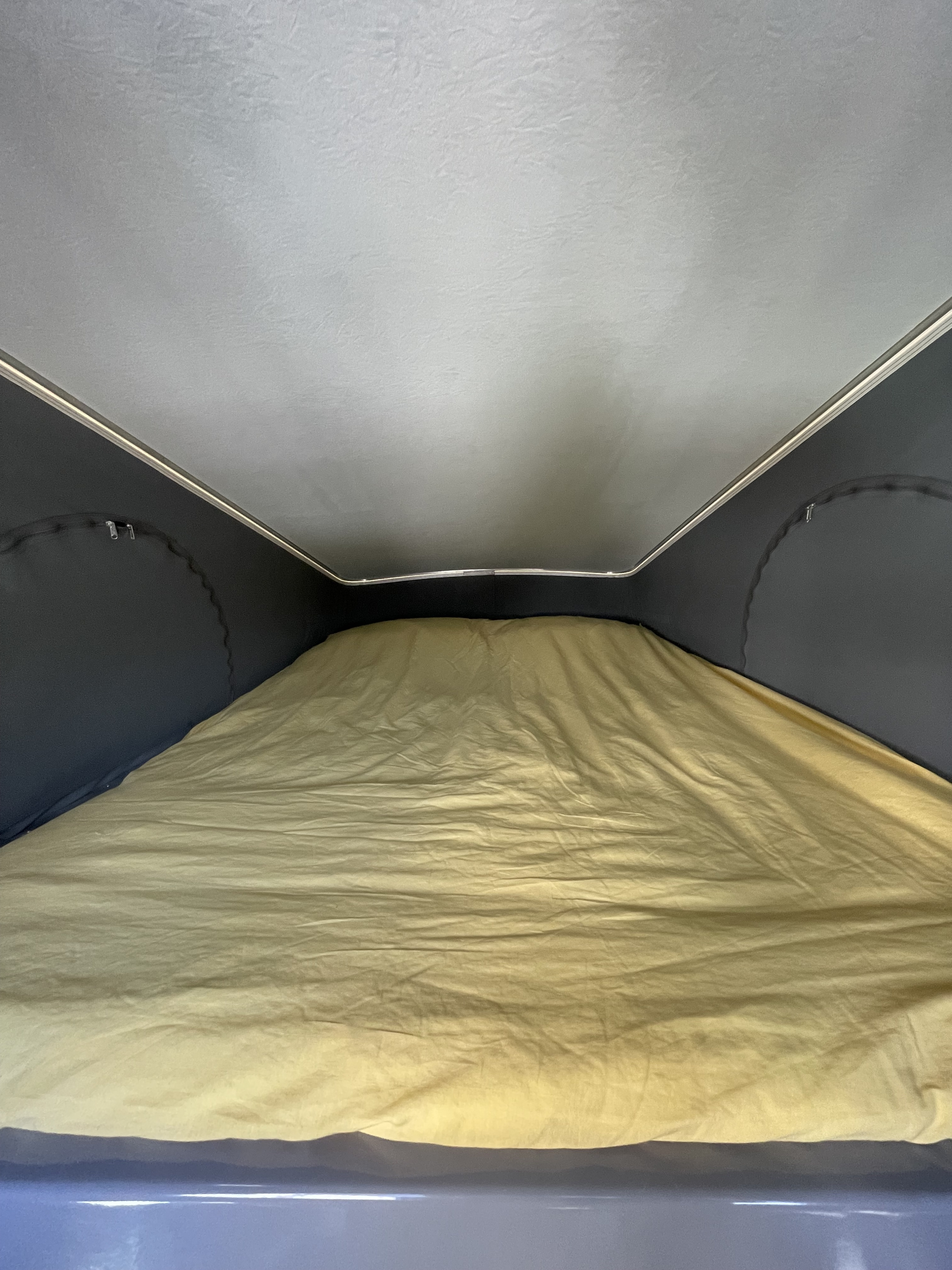 Inside an RV rental pop-top, a cozy sleeping area features a light grey ceiling and yellow bedding, perfect for trips.. Winnebago Solis 2023