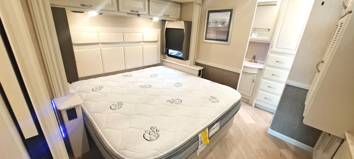 Modern RV rental bedroom with a large bed, padded headboard, built-in storage, and a compact sink area.. Fleetwood BOUNDER 35k 2021