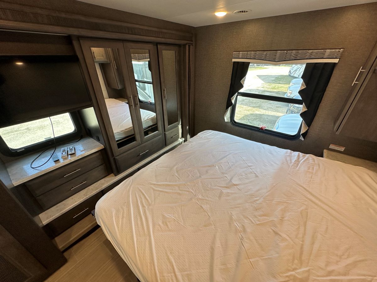 Modern RV rental bedroom interior with a comfortable bed, mirrored closet, TV, and large window.. Thor 35MQ 2022
