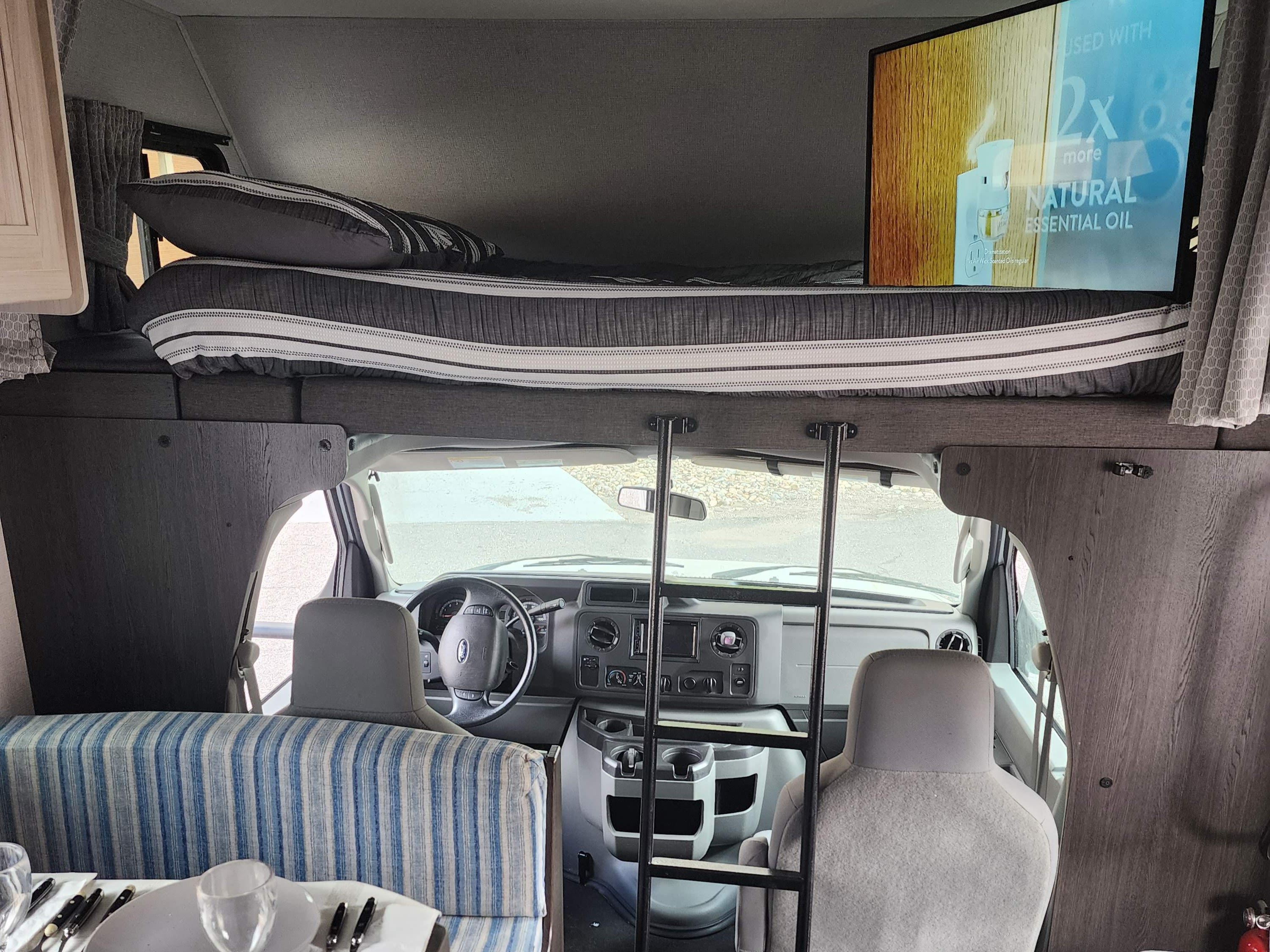 Inside this RV rental: spacious overhead bunk with ladder, driver's cockpit, and dining booth with striped cushions.. Forest River Forester 2020