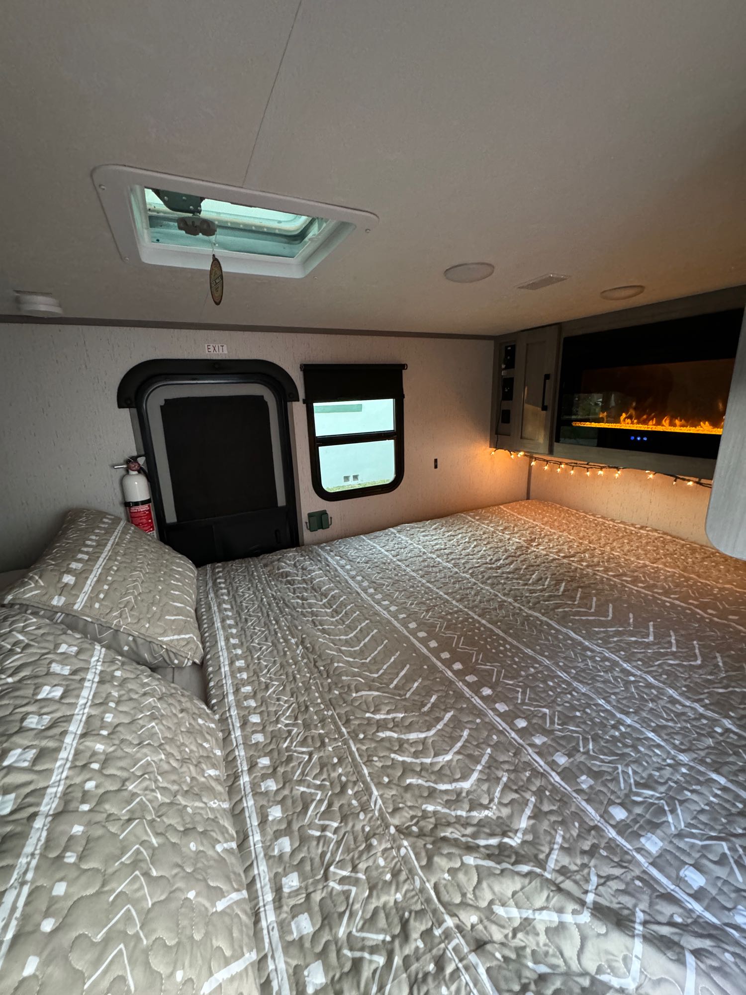 Cozy RV rental bedroom with patterned bed, TV fireplace, window, emergency exit, and fire extinguisher visible.. Dutchmen Other 2023