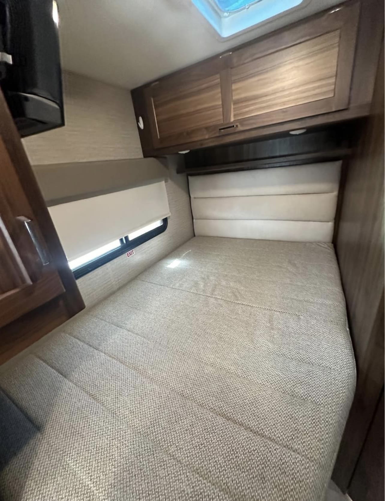 RV rental bedroom featuring a spacious bed with padded headboard, window with blind, and overhead cabinets for storage.. Winnebago Minnie Winnie 2022