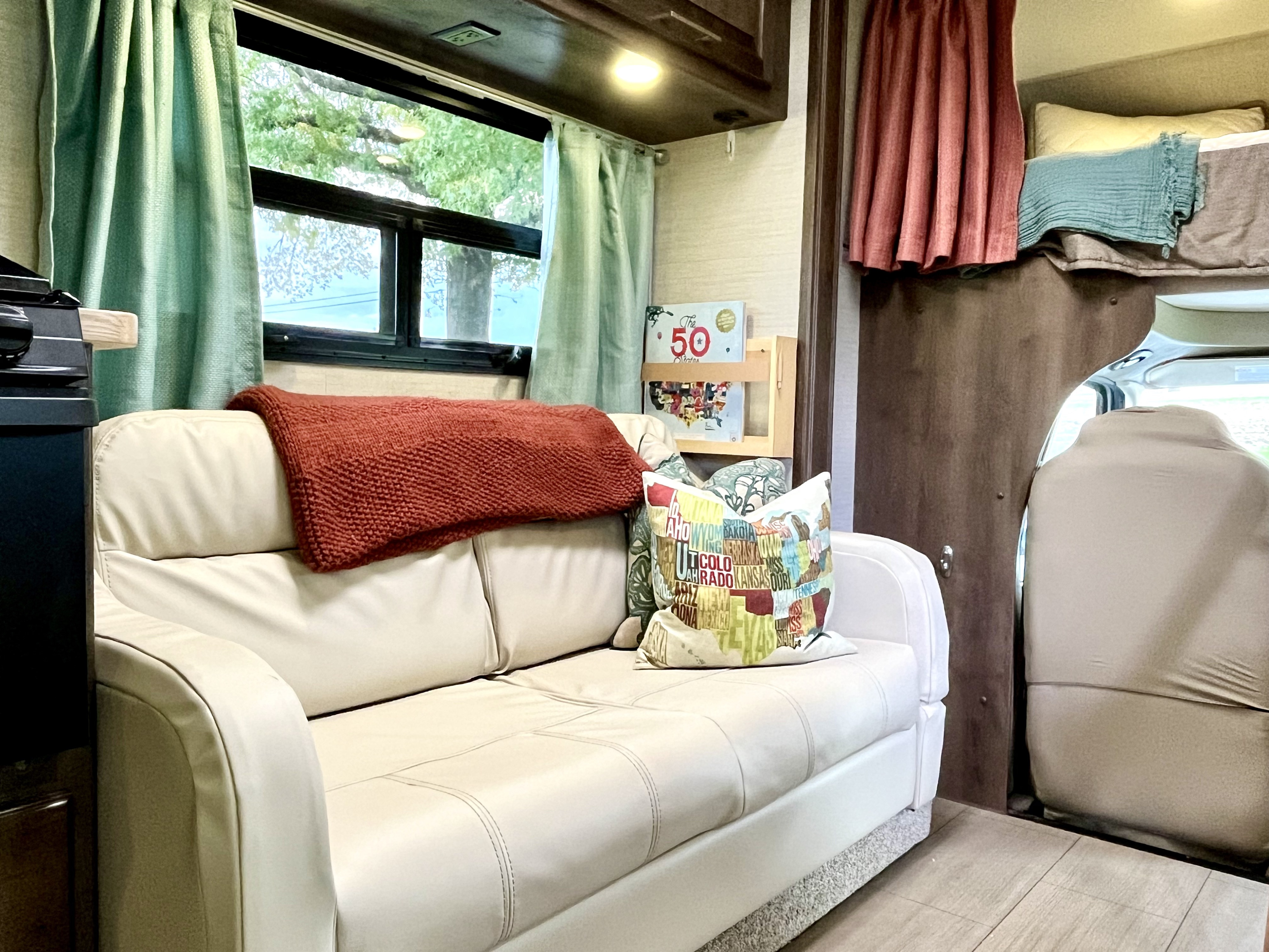 Cozy RV rental interior featuring a comfortable sofa, window with green curtains, and a bunk bed, perfect for travel adventures.. Jayco Greyhawk 2018