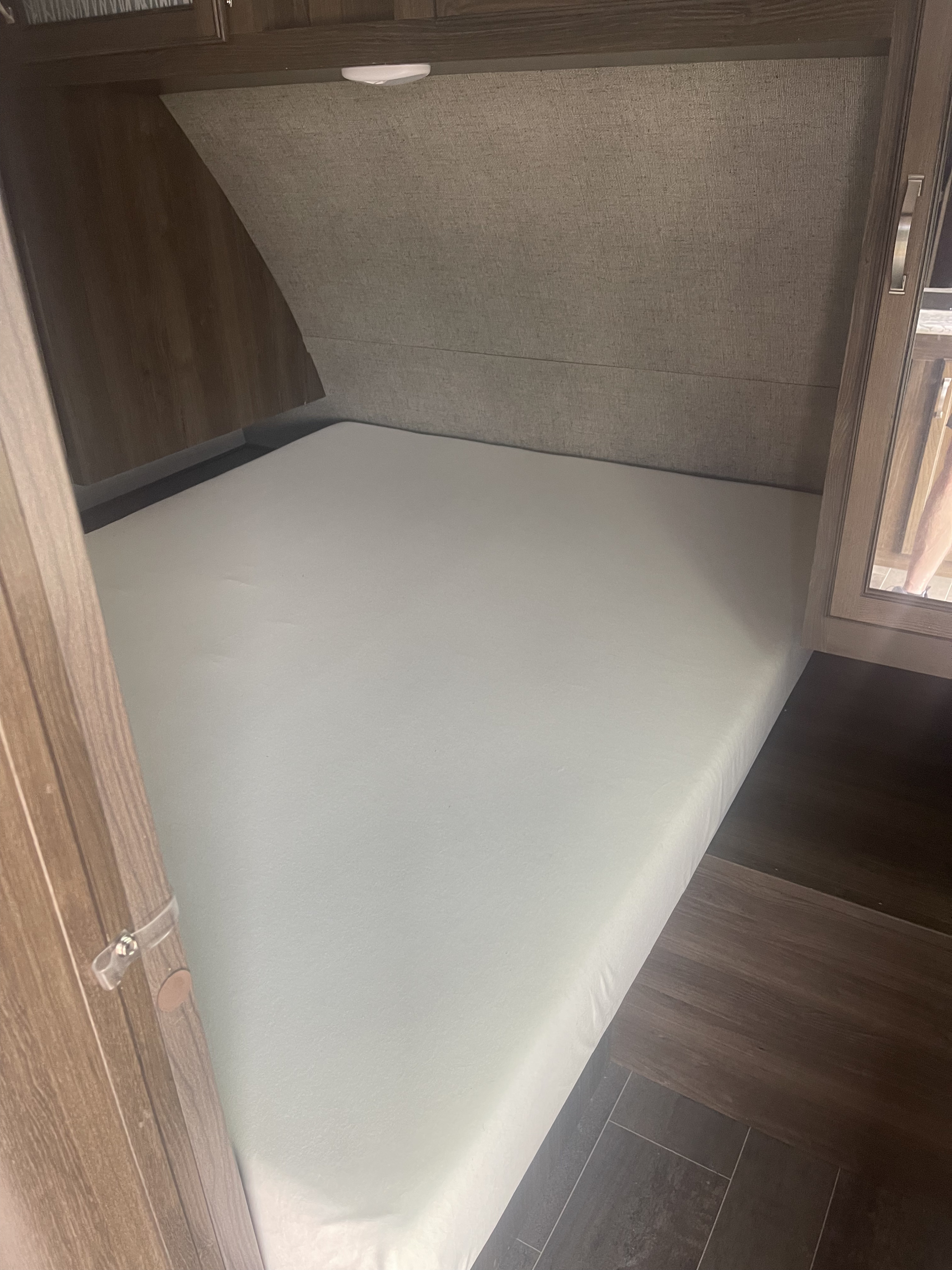 Inside a well-appointed RV rental bedroom, featuring a pristine white mattress, textured headboard, and wood cabinetry.. Keystone RV Bullet Ultra Lite 2018